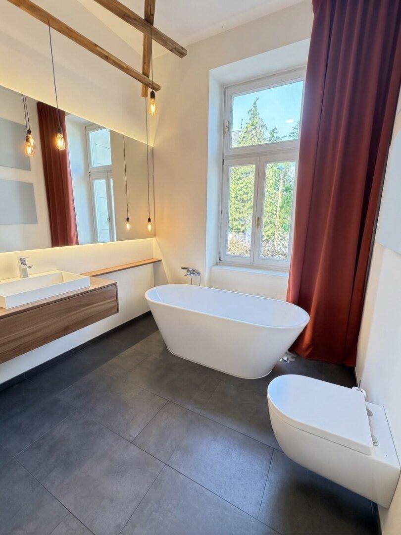 Luxuriöses Badezimmer mit freistehender Badewanne, Doppelwaschbecken und großen Fenstern.