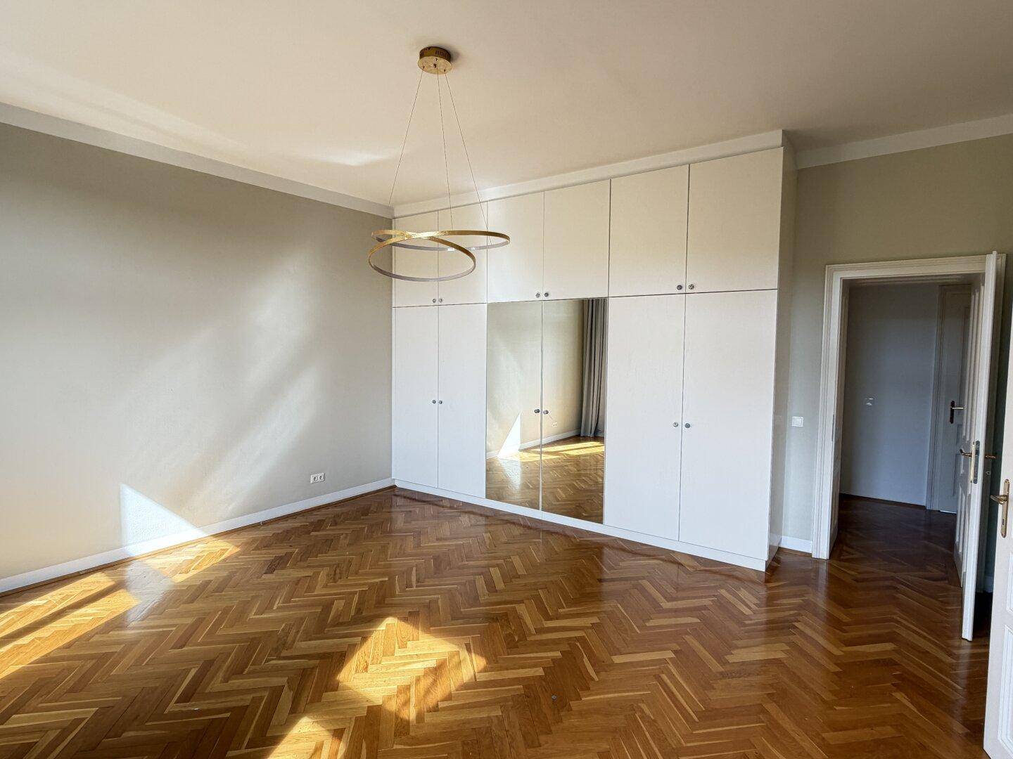 Geräumiges Schlafzimmer mit Fischgrätparkett, Einbauschränken und Spiegelfronten.