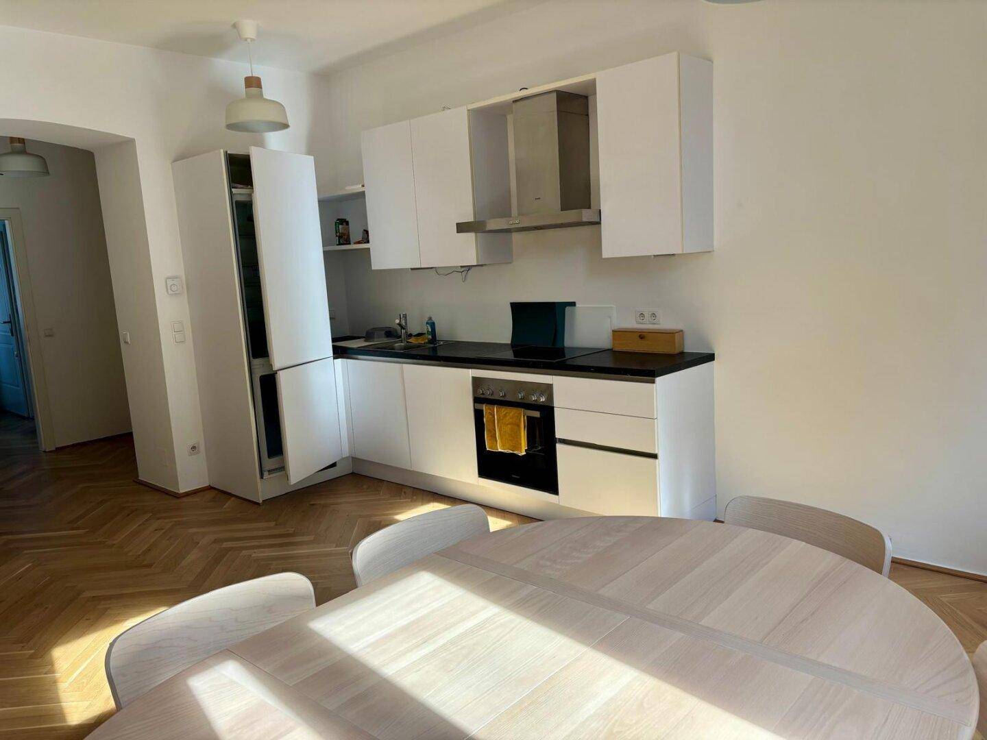 Moderne Küche mit Essbereich, weißen Schränken und integrierten Geräten, sonnendurchflutet.