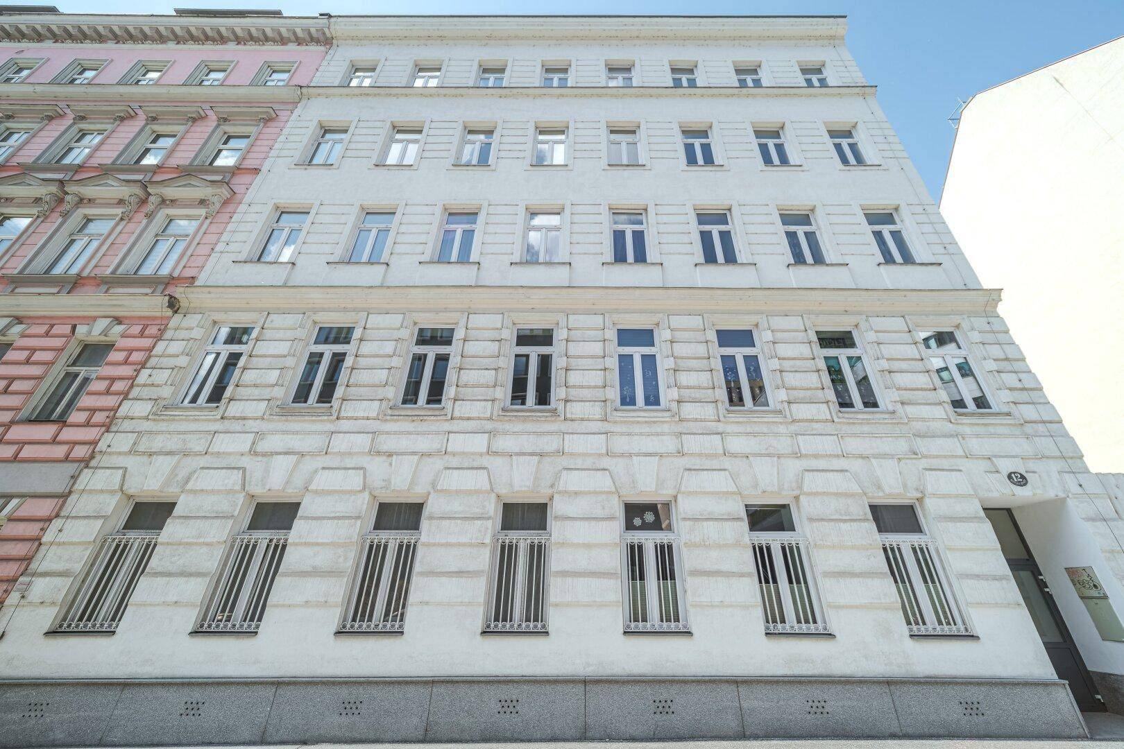 Klassische Fassade eines Mehrfamilienhauses mit vielen Fenstern und Balkonen unter blauem Himmel.