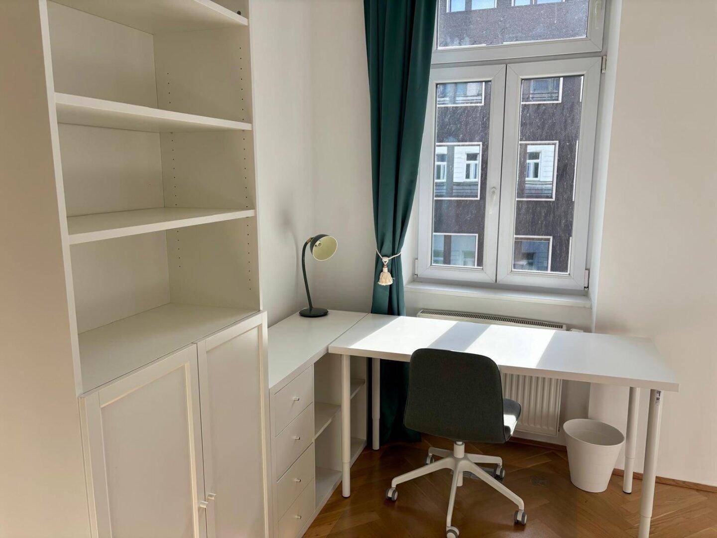 Arbeitsbereich mit Schreibtisch, Bürostuhl und Regal, gut beleuchtet durch ein großes Fenster.