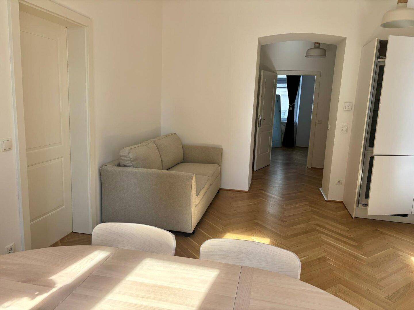 Offener Wohn-Essbereich mit Sofa, Esstisch und Zugang zu weiteren Räumen, sonnendurchflutet.