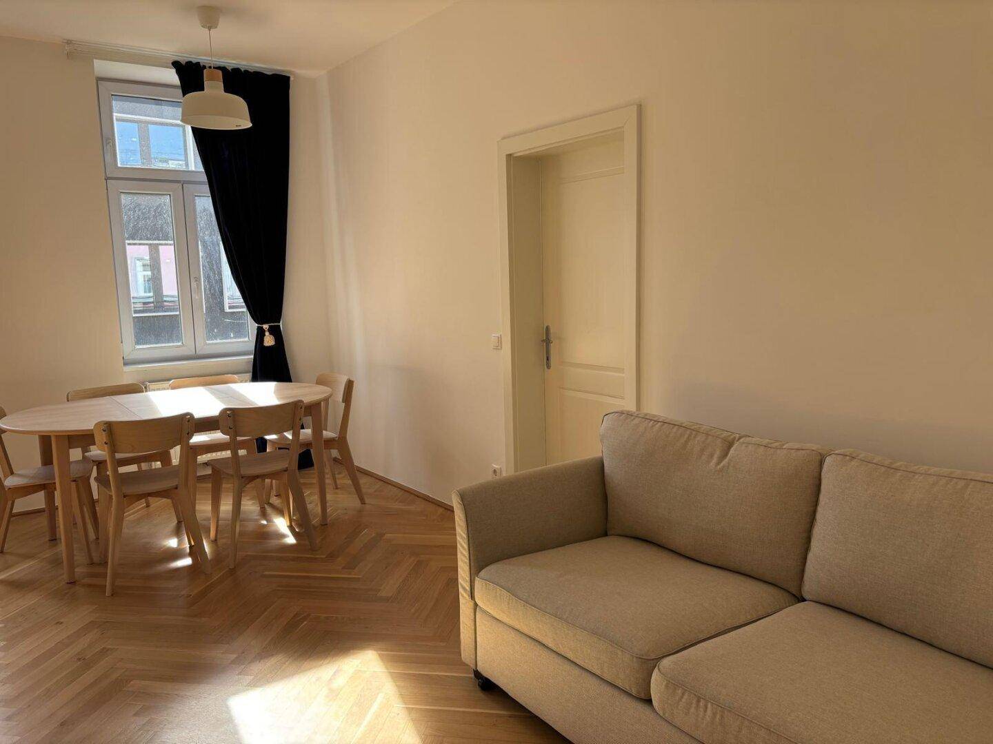 Heller Wohn-Essbereich mit Sofa, Esstisch und Parkettboden, sonnendurchflutet.