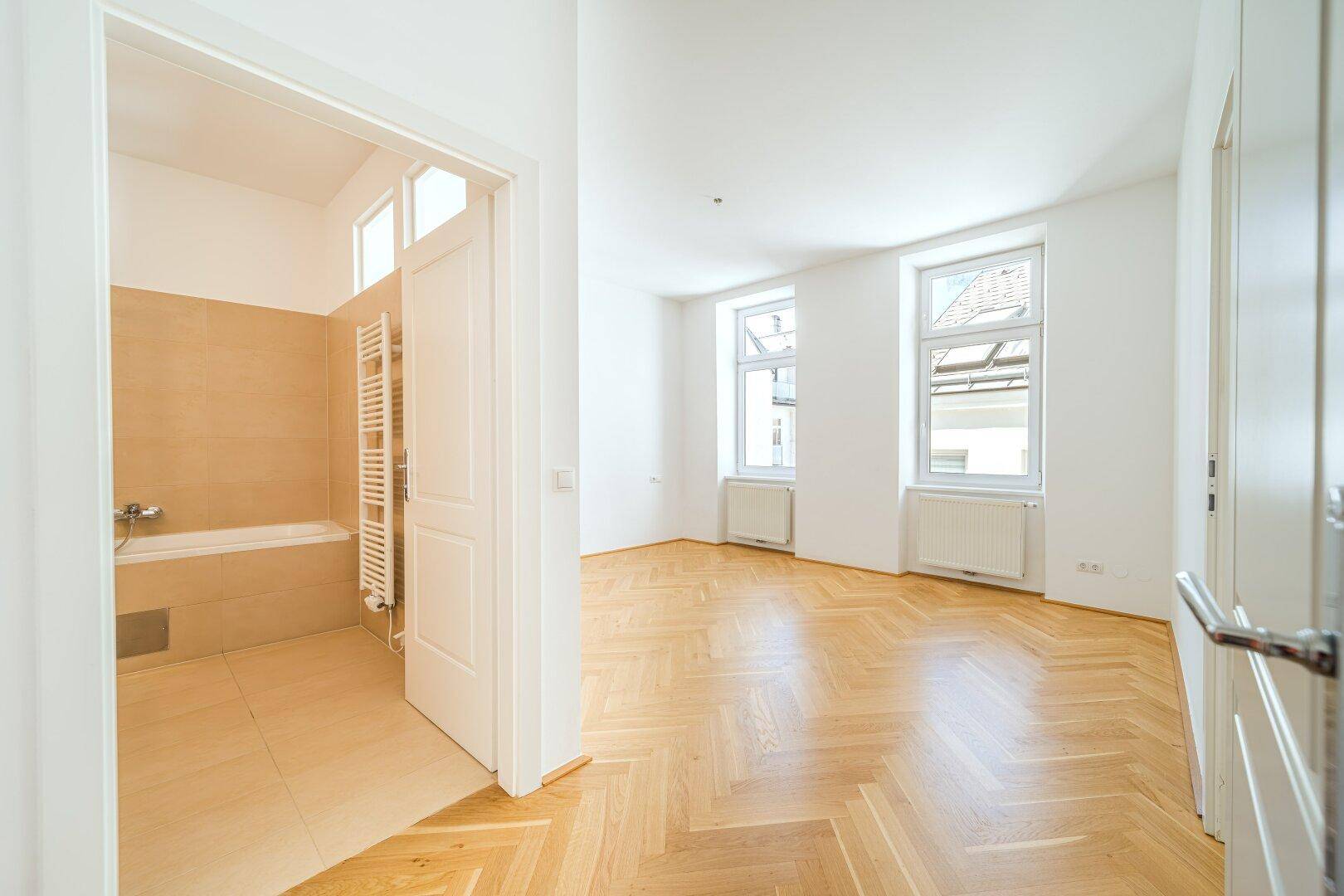 Heller Wohnraum mit Parkettboden und Blick auf die Dächer, angrenzend an ein Badezimmer.