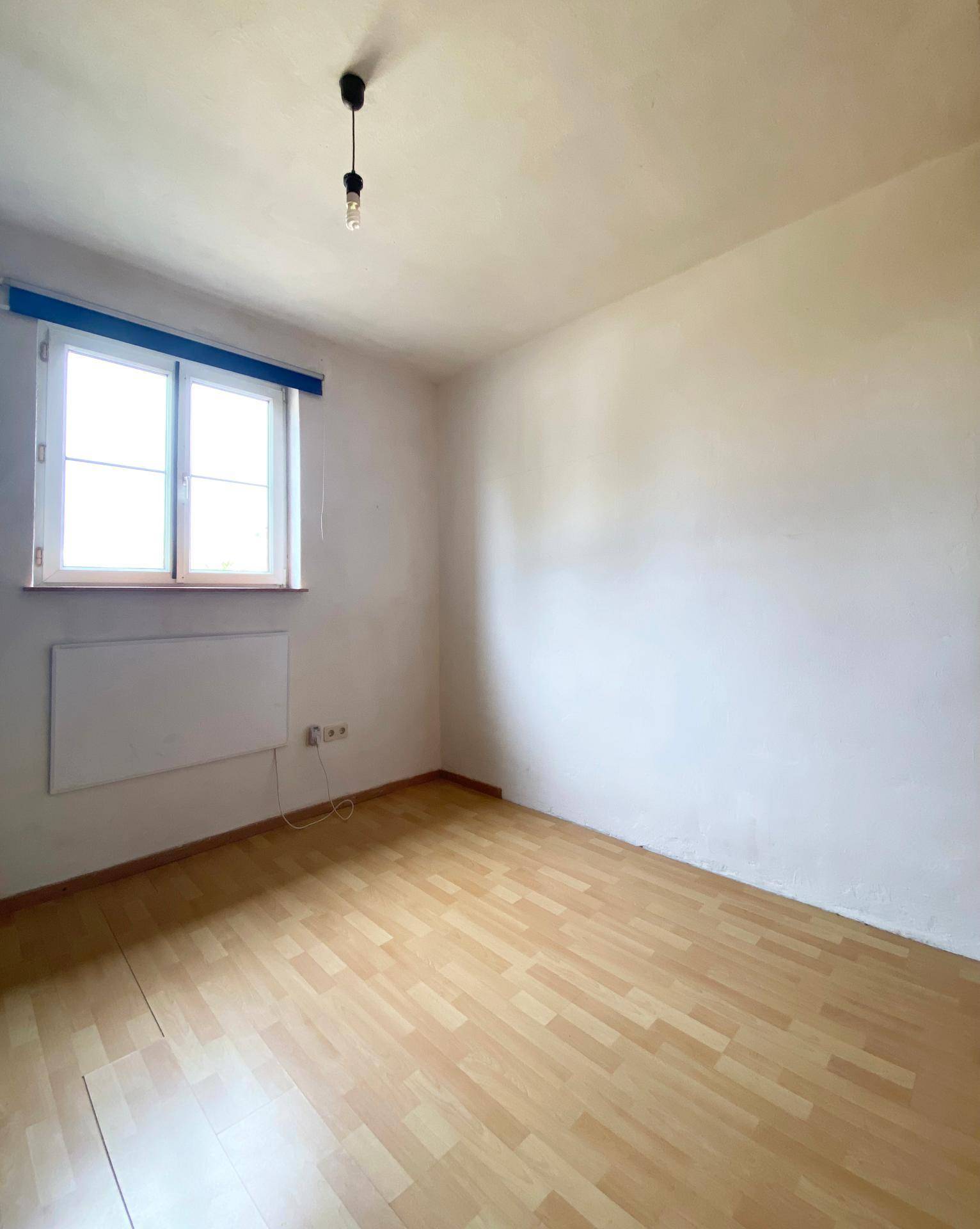 Schlafzimmer mit hellem Laminatboden und einem Fenster, das viel Tageslicht hereinlässt.