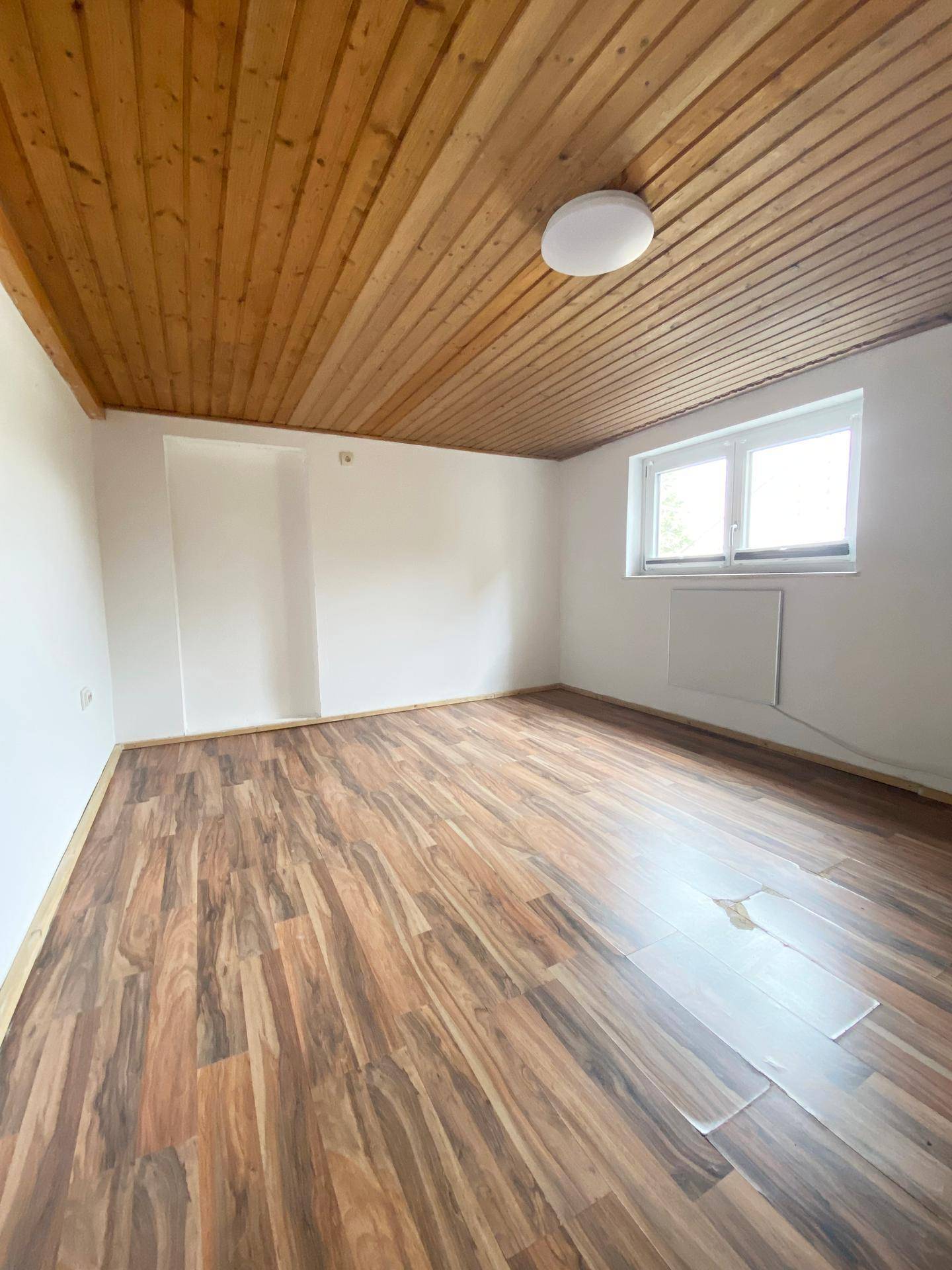 Gemütliches Schlafzimmer mit dunklem Laminatboden und einer warmen Holzdeckenverkleidung.