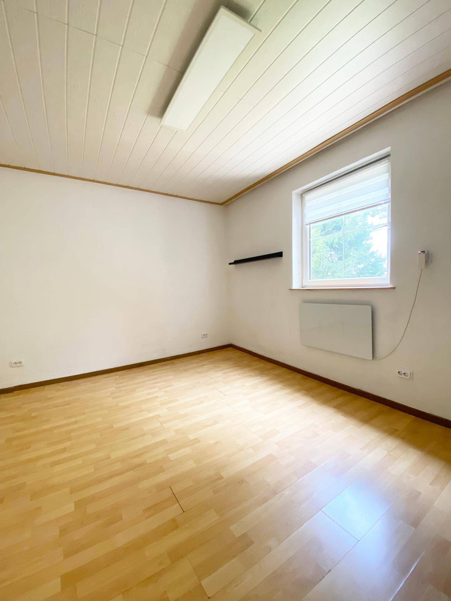 Schlafzimmer mit hellem Laminatboden und einem Fenster, das den Raum mit natürlichem Licht füllt.