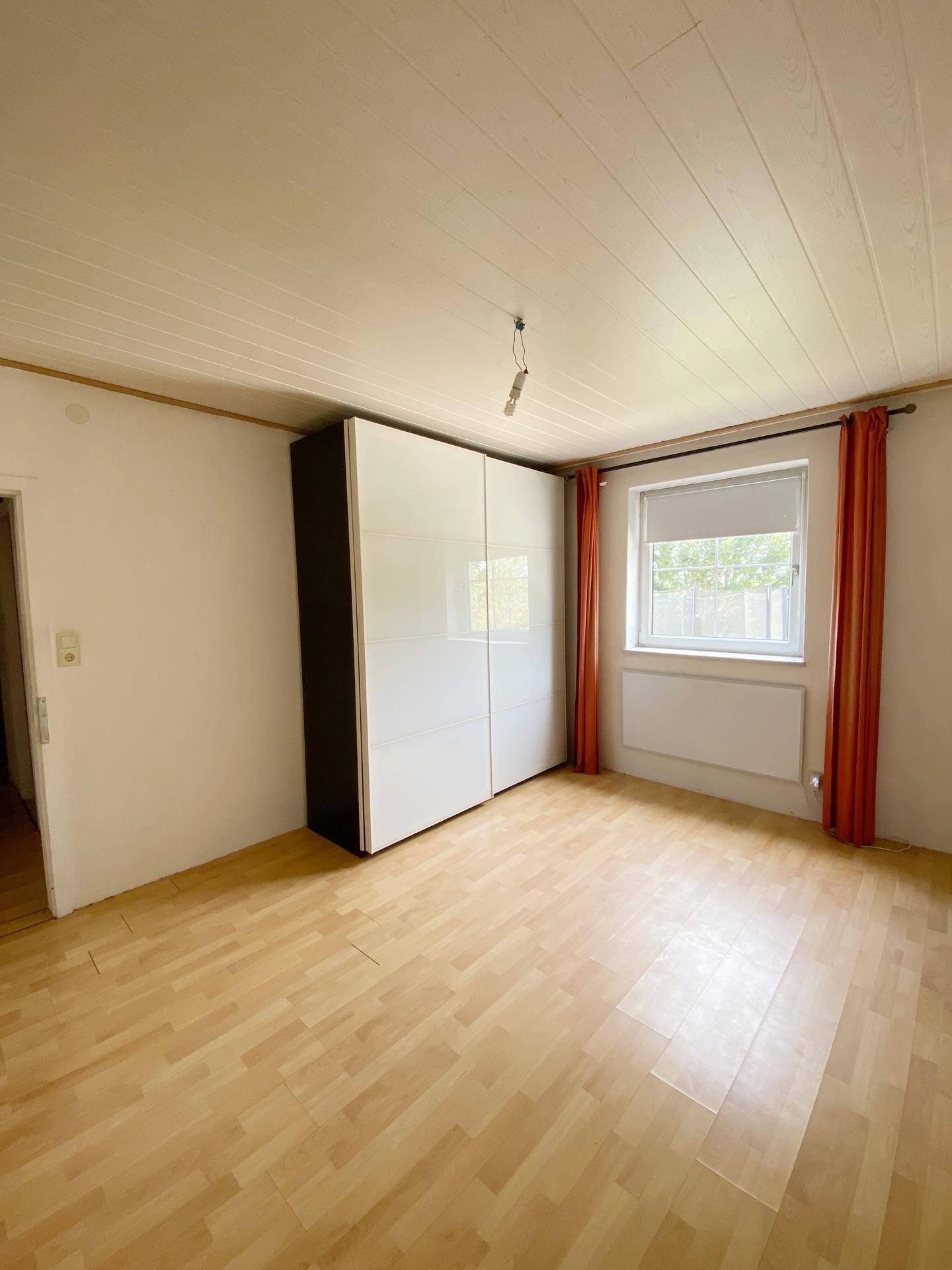 Schlafzimmer mit hellem Laminatboden, weißer Deckenverkleidung und einem großen Kleiderschrank.
