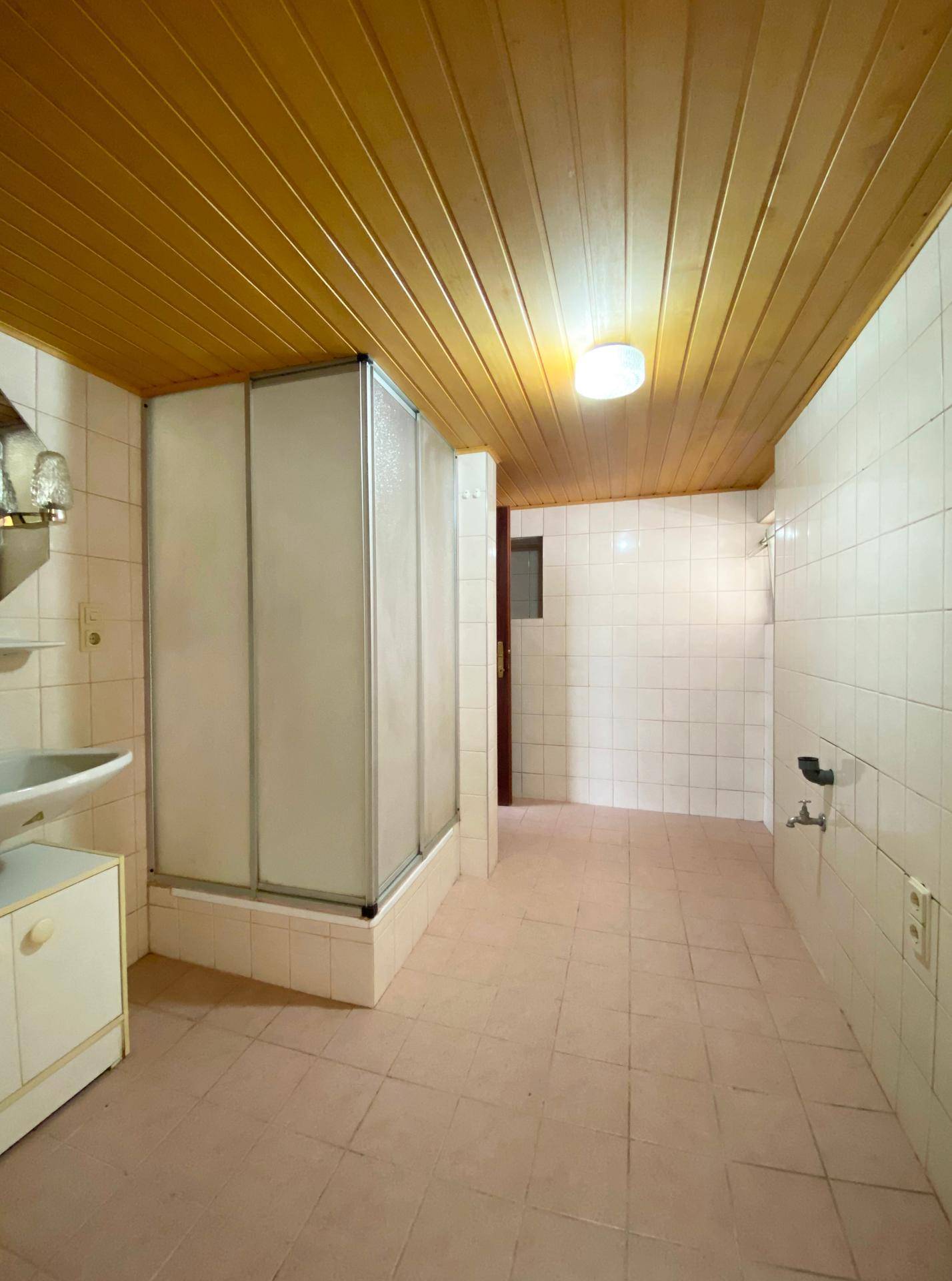 Badezimmer mit Duschkabine, hellen Fliesen und einer Holzdeckenverkleidung im Landhausstil.
