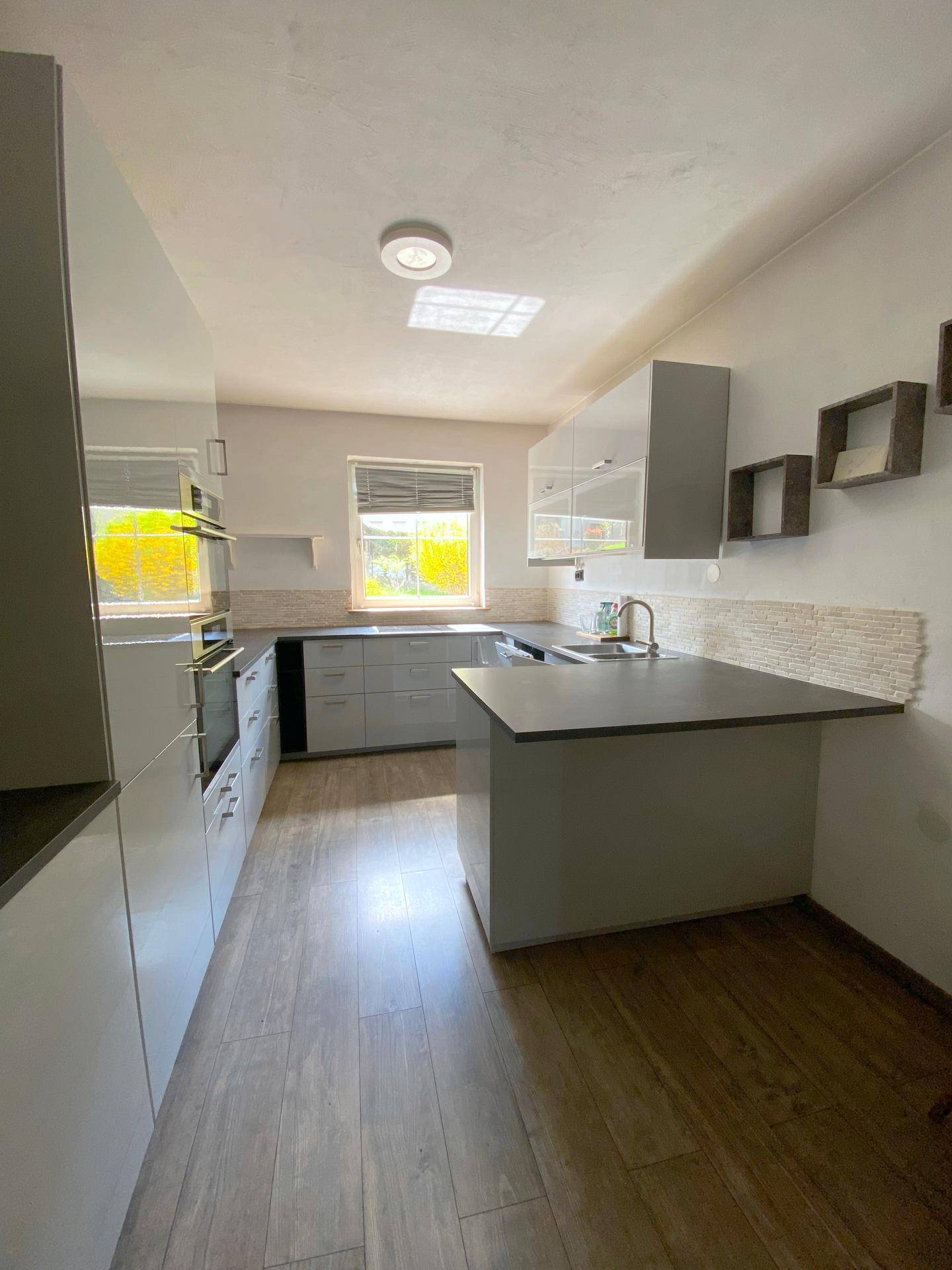 Moderne Einbauküche mit grauen Hochglanzfronten, dunklen Arbeitsplatten und Holzoptik-Laminatboden.