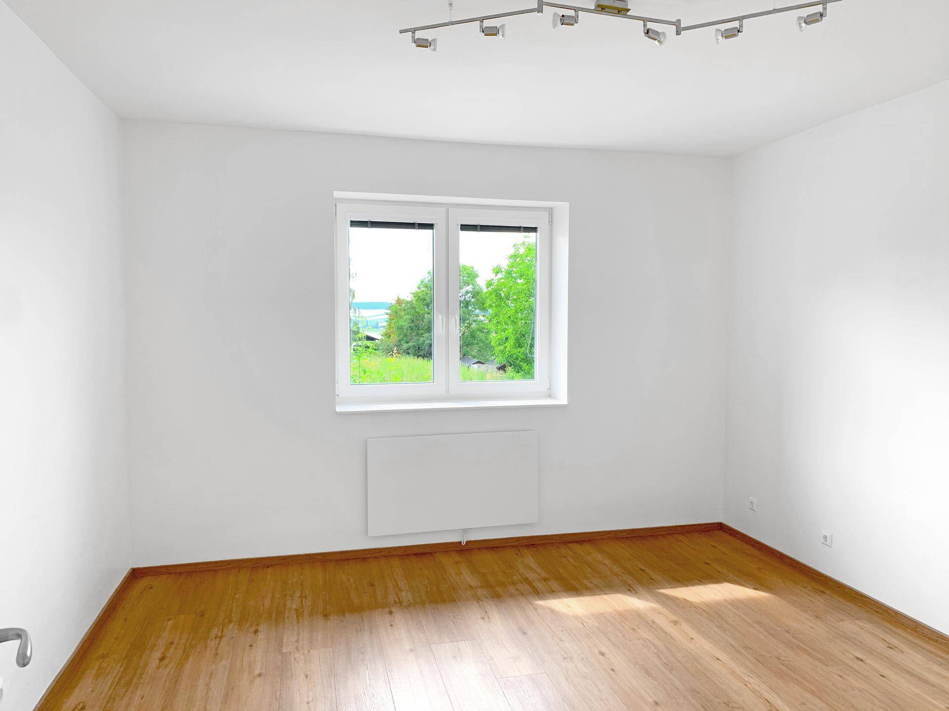 Helles Schlafzimmer mit Holzboden und großem Fenster mit Blick ins Grüne.