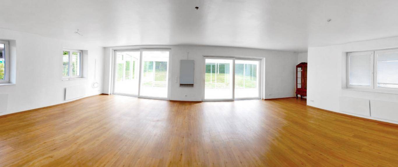 Geräumiges Wohnzimmer mit hellem Holzboden, großen Schiebetüren und viel Tageslicht.