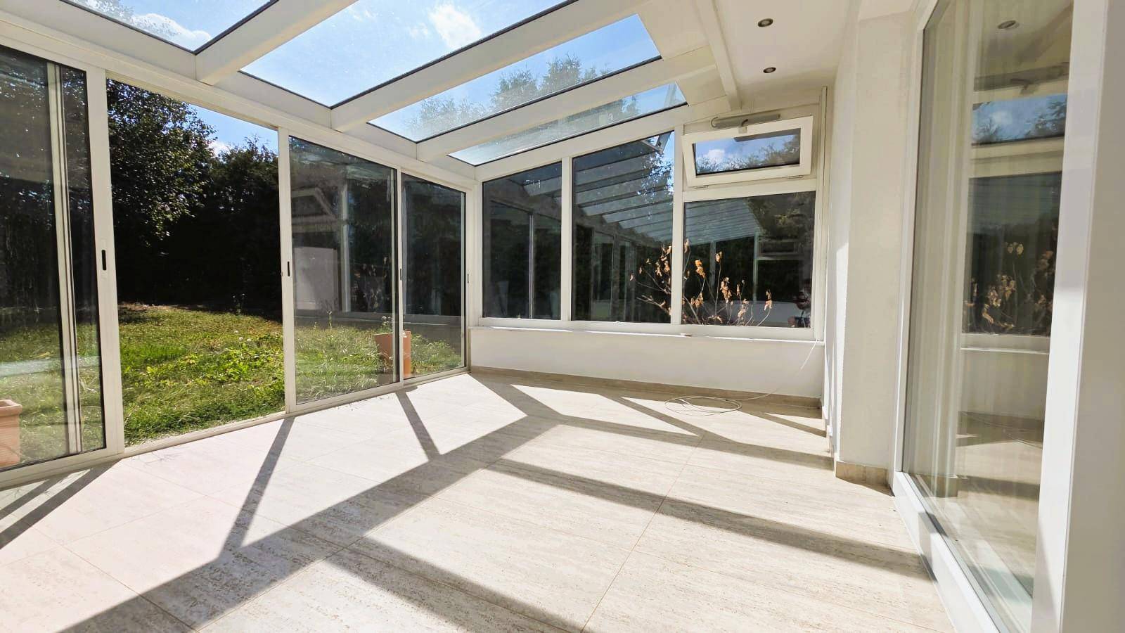Helles Zimmer mit großen Glasflächen, Fliesenboden und Blick in den Garten.
