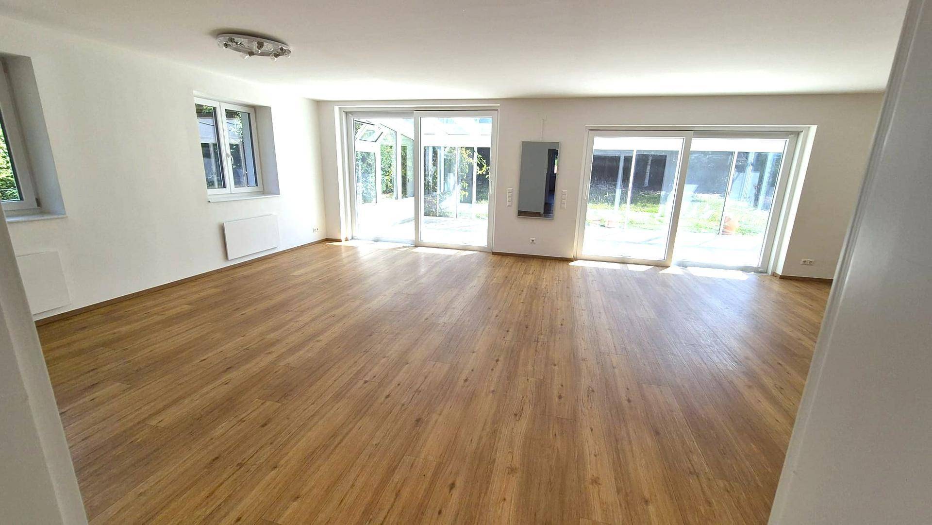 Geräumiges, leeres Wohnzimmer mit Holzboden und Zugang zu einer Terrasse oder Garten.