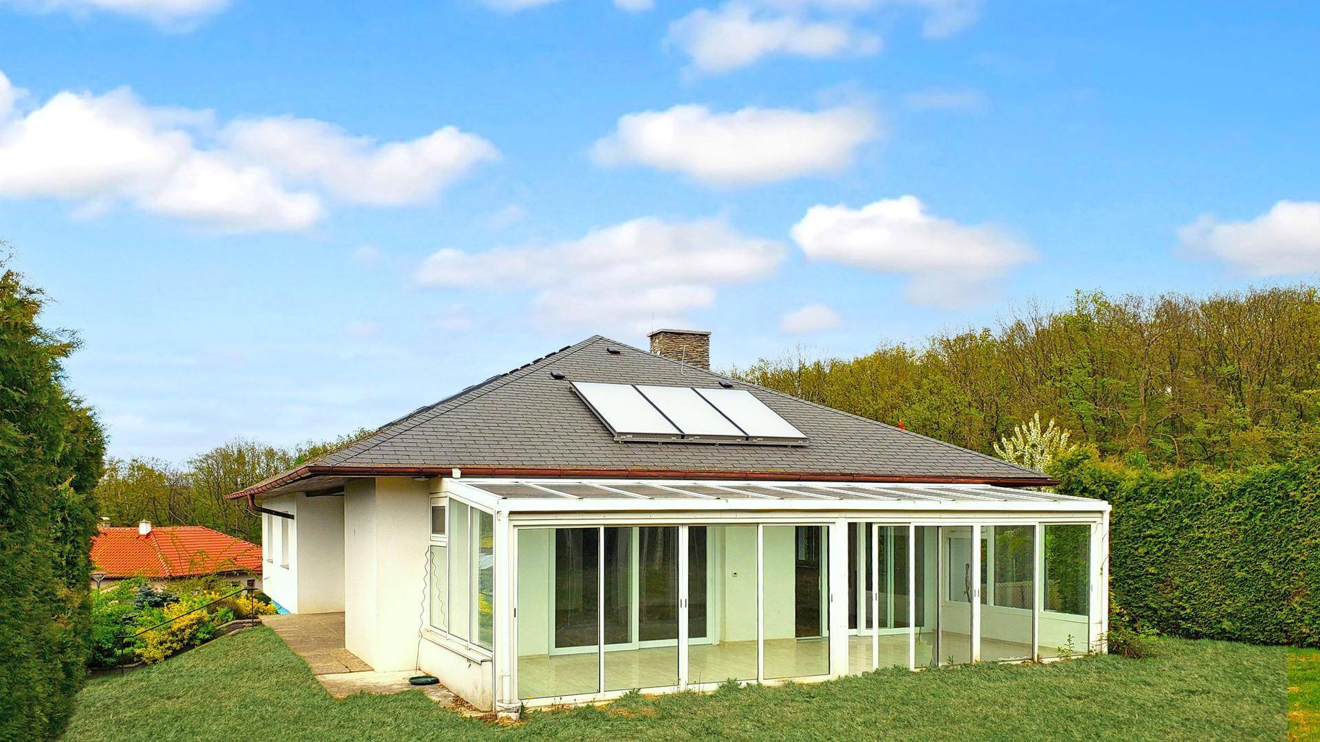 Rückseite des Hauses mit großem Wintergarten, Solaranlage auf dem Dach und Garten.