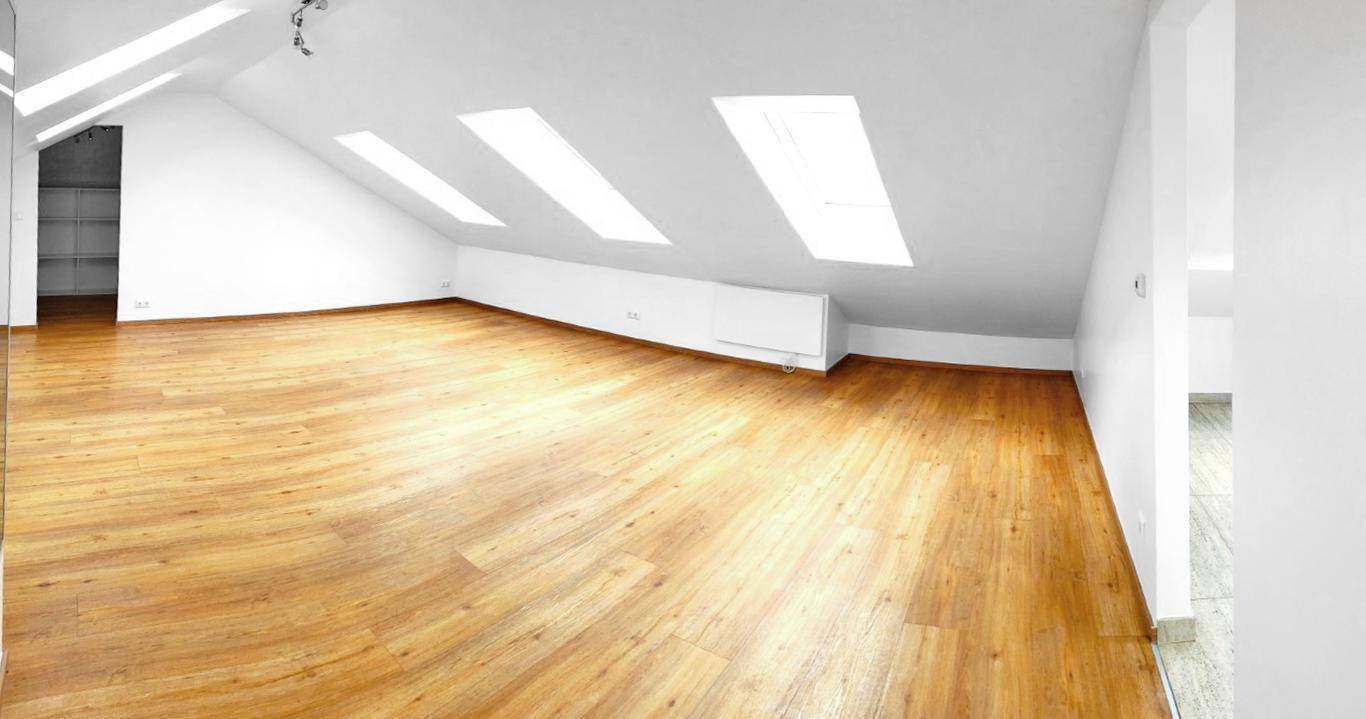 Heller Dachbodenraum mit Holzboden, schrägen Wänden und Dachfenstern für viel Licht.