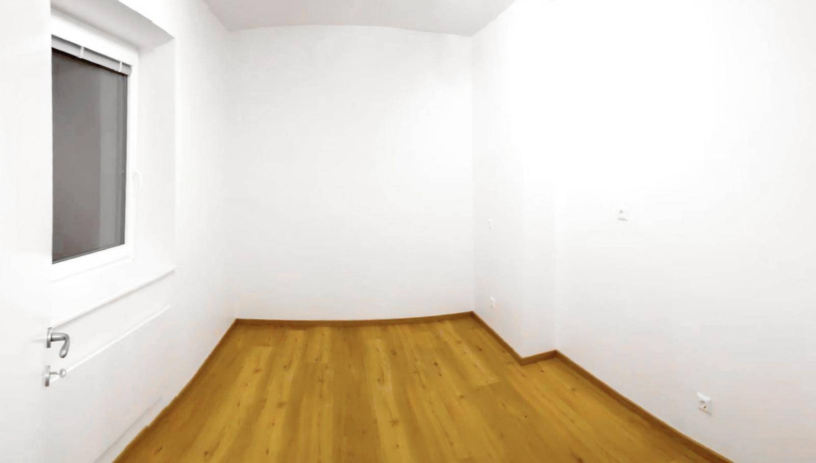 Kleines, helles Zimmer mit Holzboden und einem Fenster, ideal als Kinder- oder Gästezimmer.