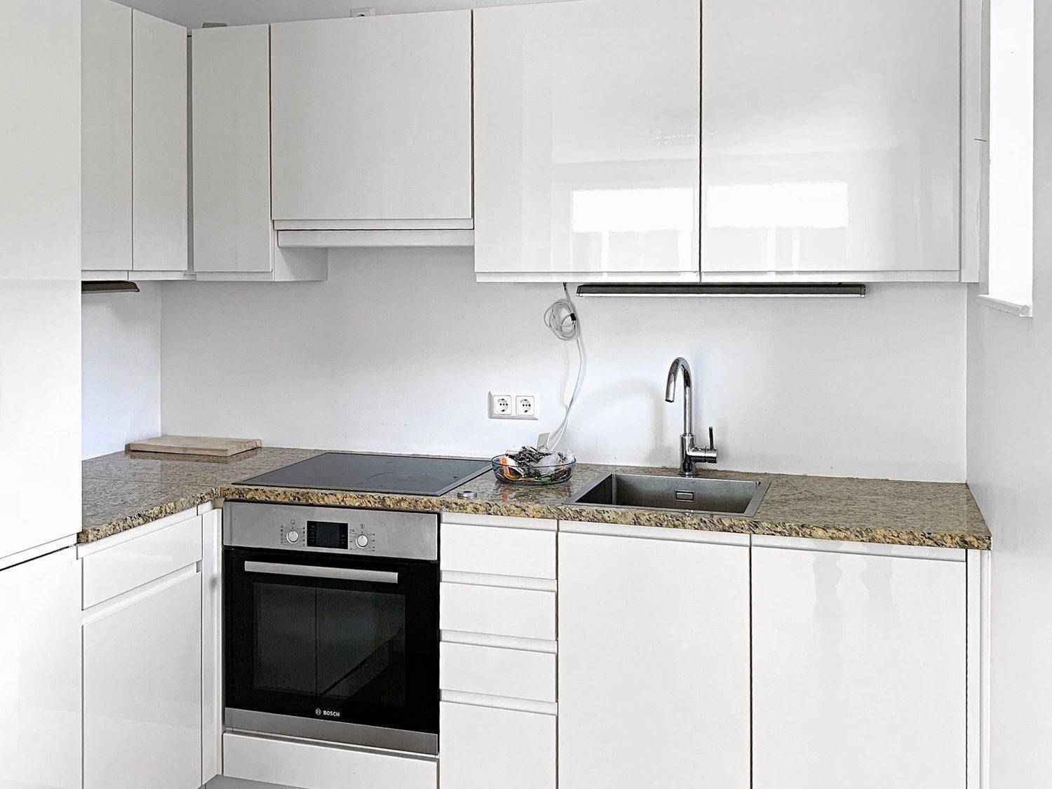 Moderne Einbauküche mit weißen Hochglanzfronten, Granitarbeitsplatte und Bosch-Geräten.
