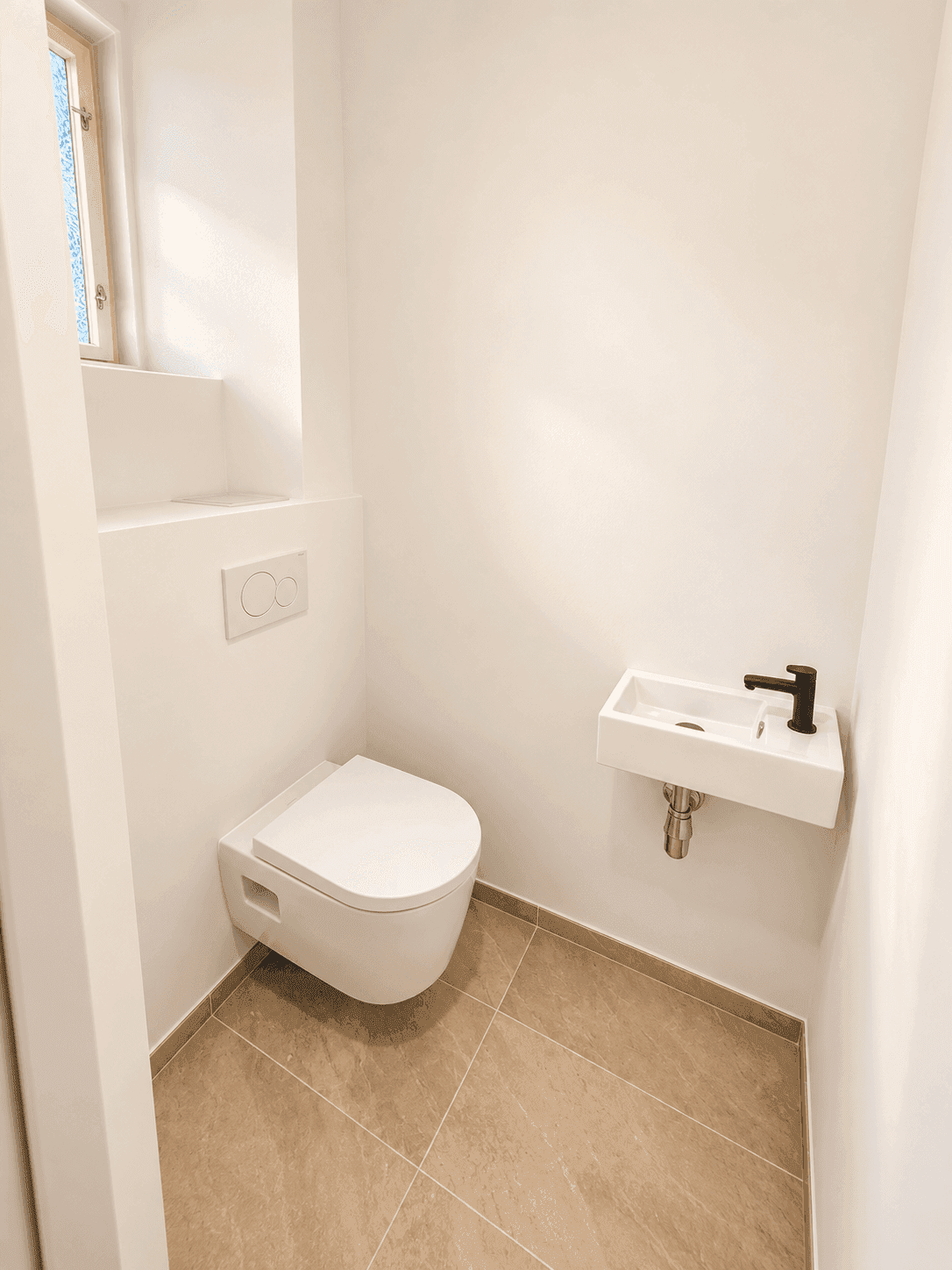 Modernes Gäste-WC mit wandhängender Toilette, kleinem Waschbecken und Fliesenboden.