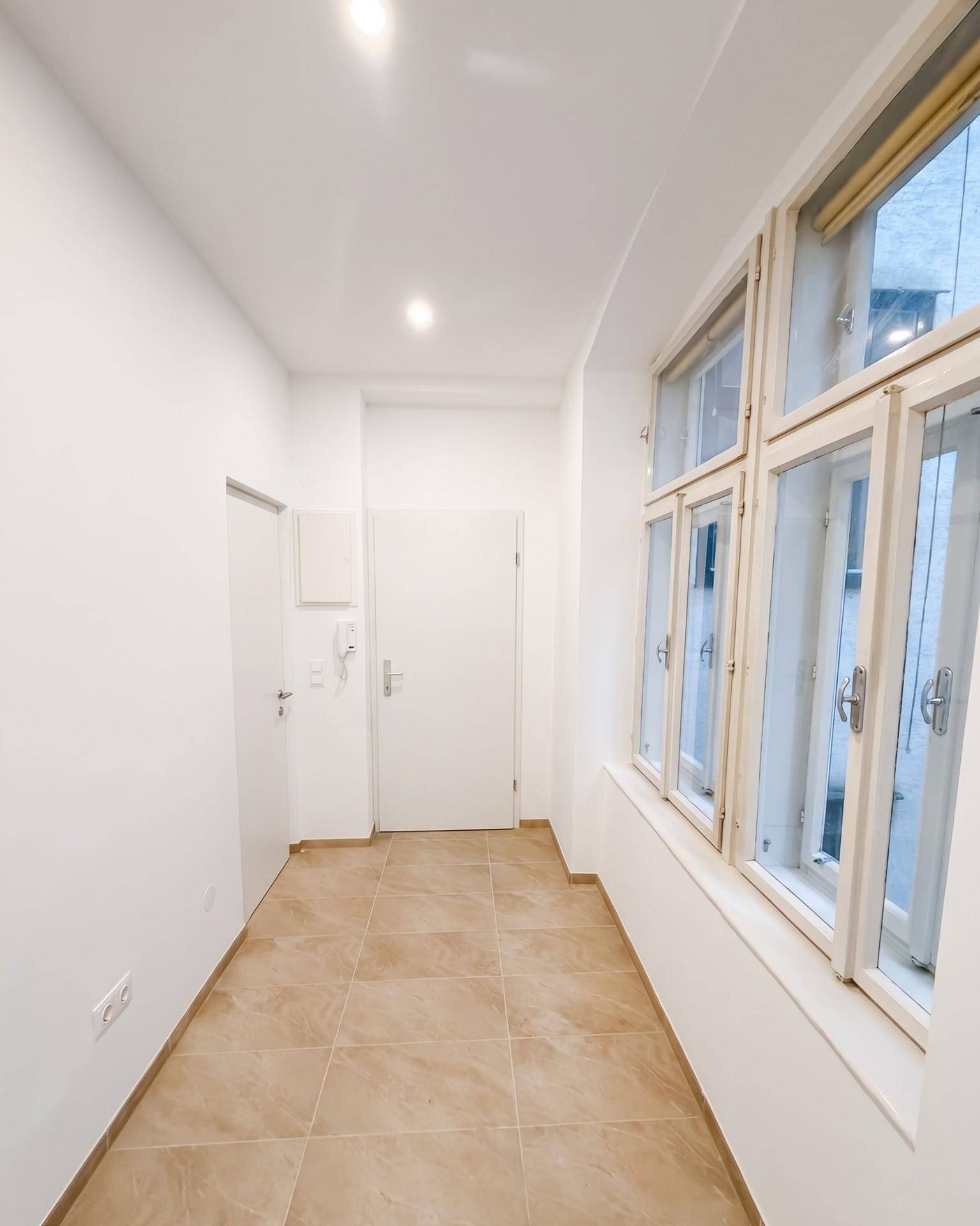 Eingangsbereich mit Fliesenboden, Gegensprechanlage und großen Fenstern, die viel Licht hereinlassen.