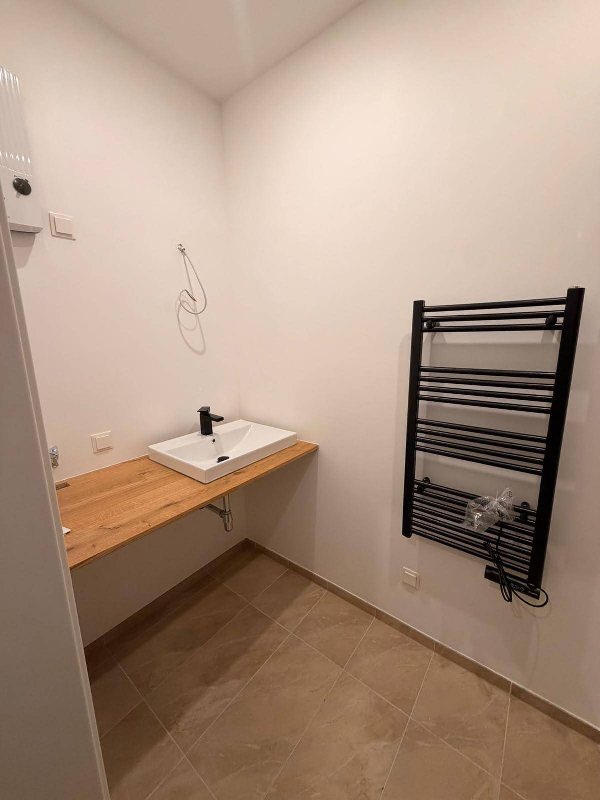 Modernes Badezimmer mit Waschbecken auf Holzplatte und schwarzem Handtuchheizkörper.