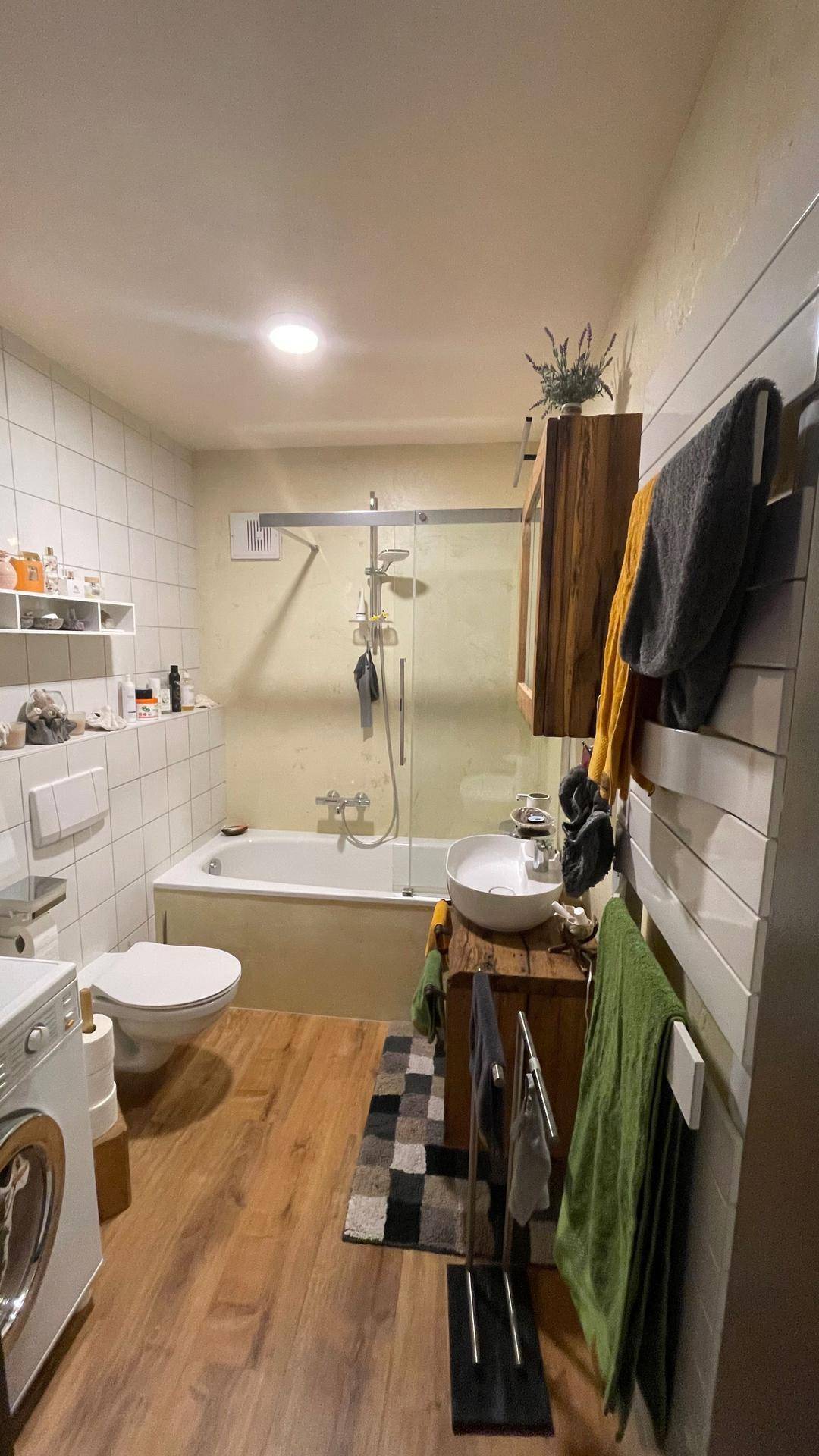 Helles Badezimmer mit Holzboden, Badewanne, Toilette und Waschmaschine.