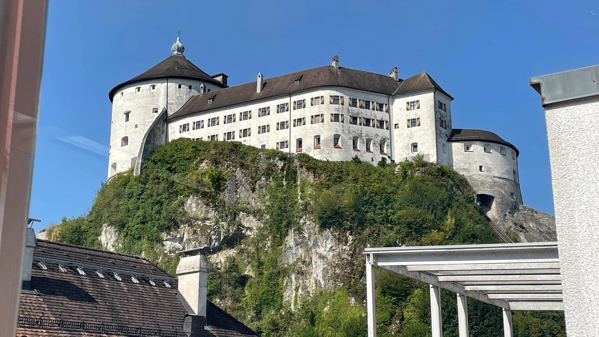 Historische Festung auf einem Felsen, umgeben von üppigem Grün unter blauem Himmel.