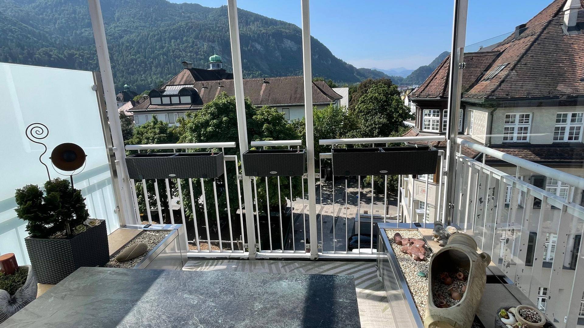 Moderner Balkon mit Glasgeländer und Bergblick, ausgestattet mit Pflanzen und einem Tisch.