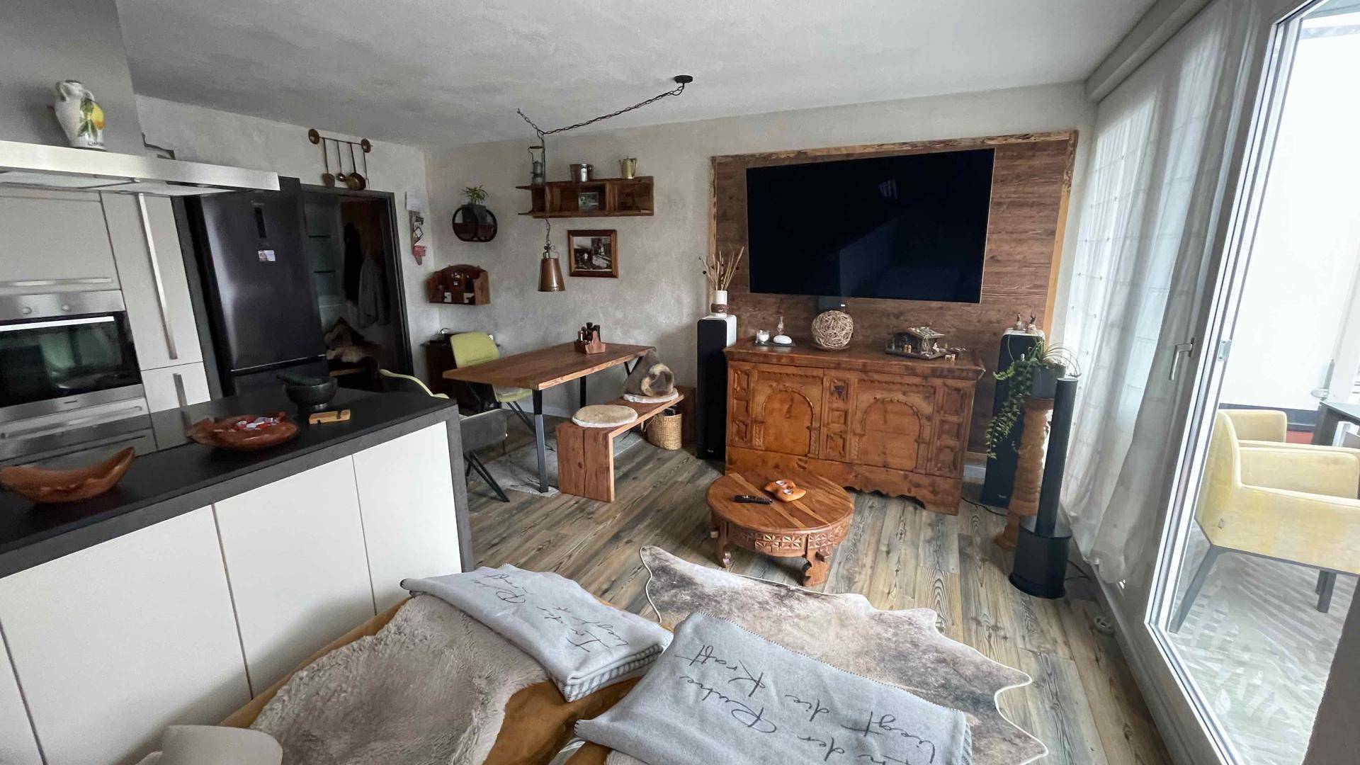 Offener Wohn-Essbereich mit integrierter Küche, Holzboden und Zugang zum Balkon.