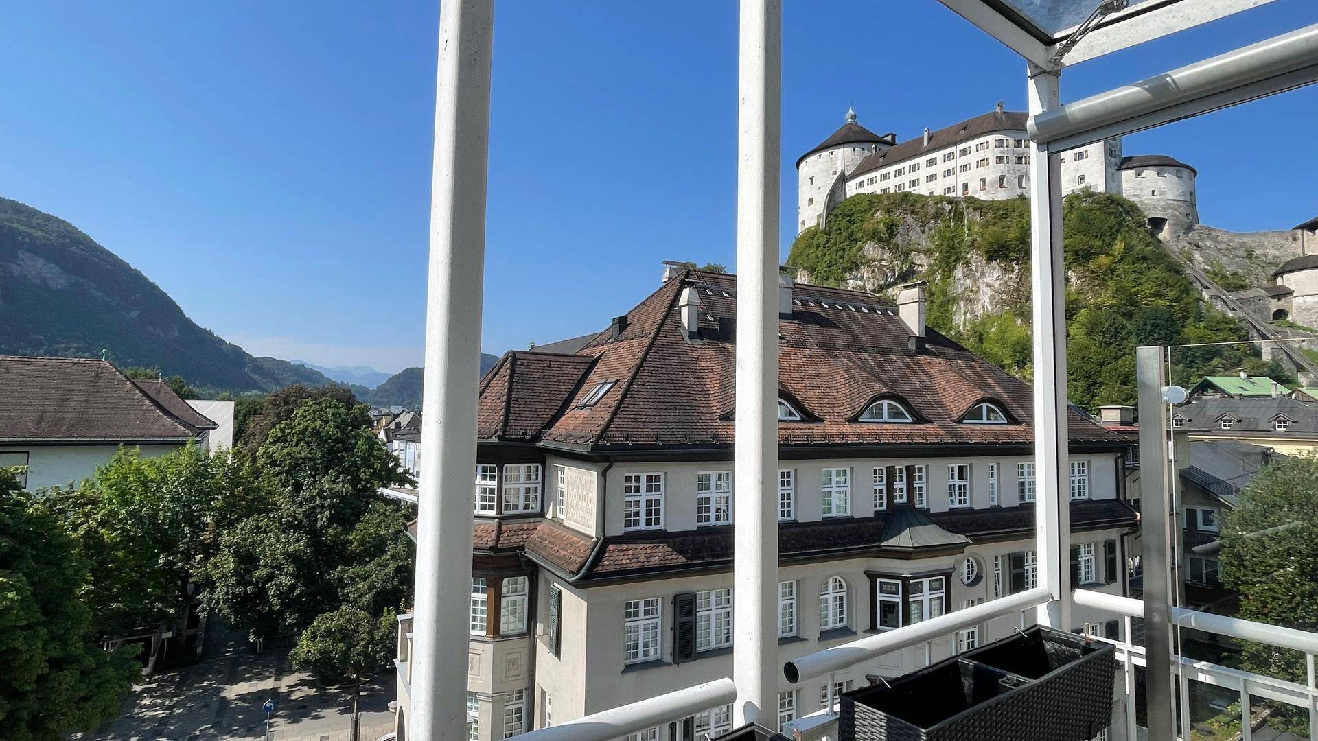 Blick vom Balkon auf ein traditionelles Gebäude mit Mansarddach und die historische Festung im Hintergrund.