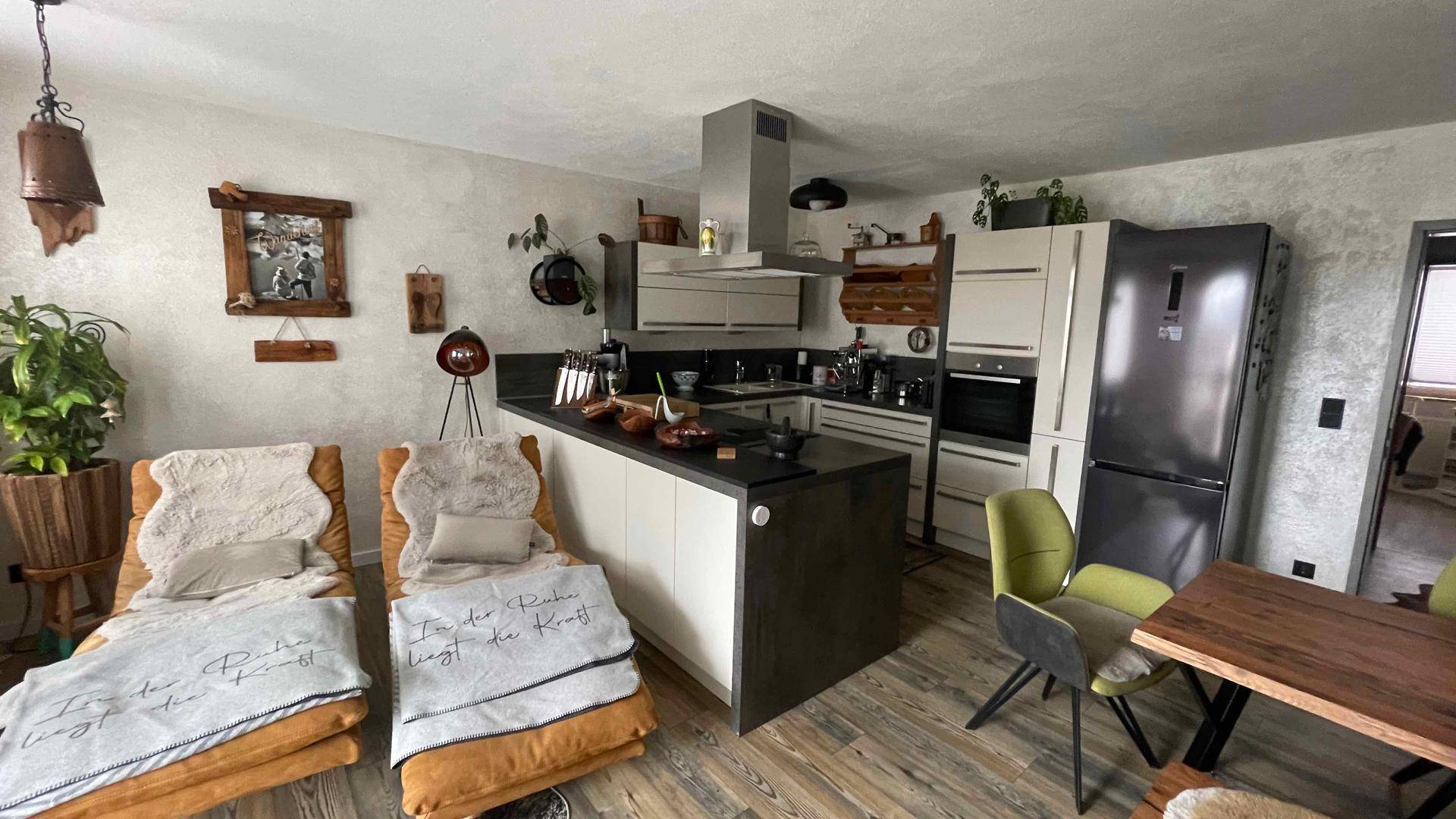 Moderne offene Küche mit Kochinsel und angrenzendem Wohnbereich mit Liegestühlen.