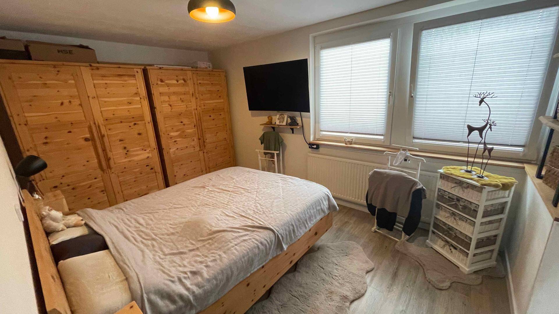 Helles Schlafzimmer mit Holzbett, Kleiderschränken und großem Fenster.