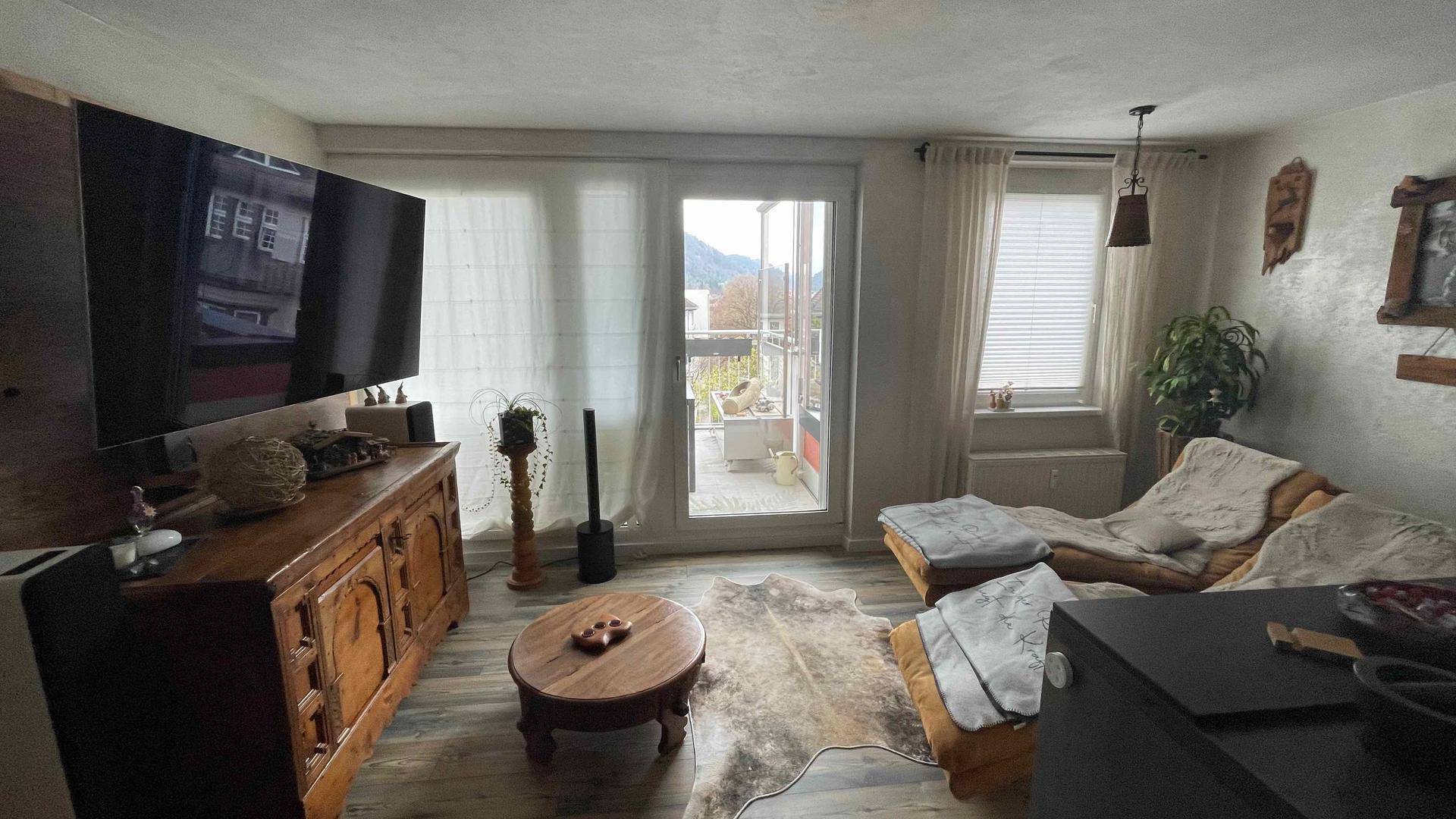 Gemütliches Wohnzimmer mit Fernseher, rustikalen Holzmöbeln und Balkonzugang.
