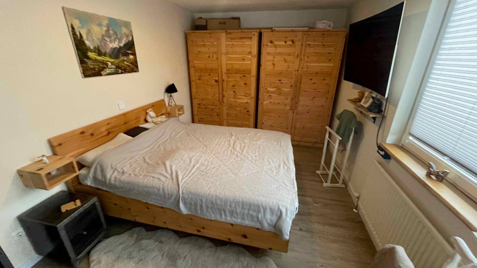 Gemütliches Schlafzimmer mit Holzbett, Einbauschränken und Fenster mit Jalousien.
