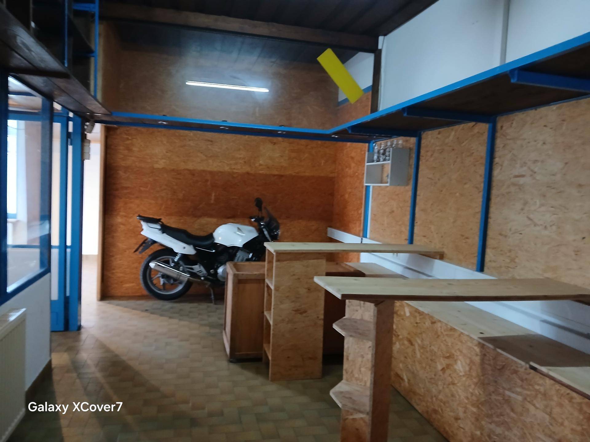 Großer Innenraum mit blauen Regalen, OSB-Wänden und einem Motorrad, das auf einer Werkstattfläche steht.