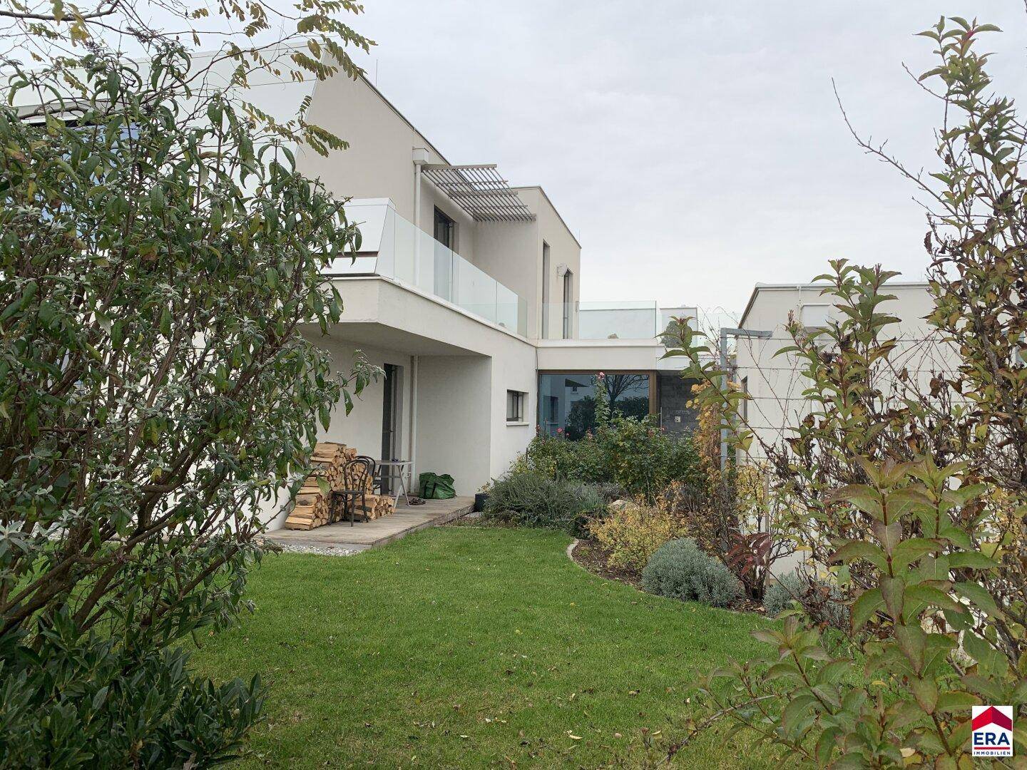 Seitlicher Blick auf die moderne Architektur des Hauses mit gepflegtem Garten und Holzstapel.