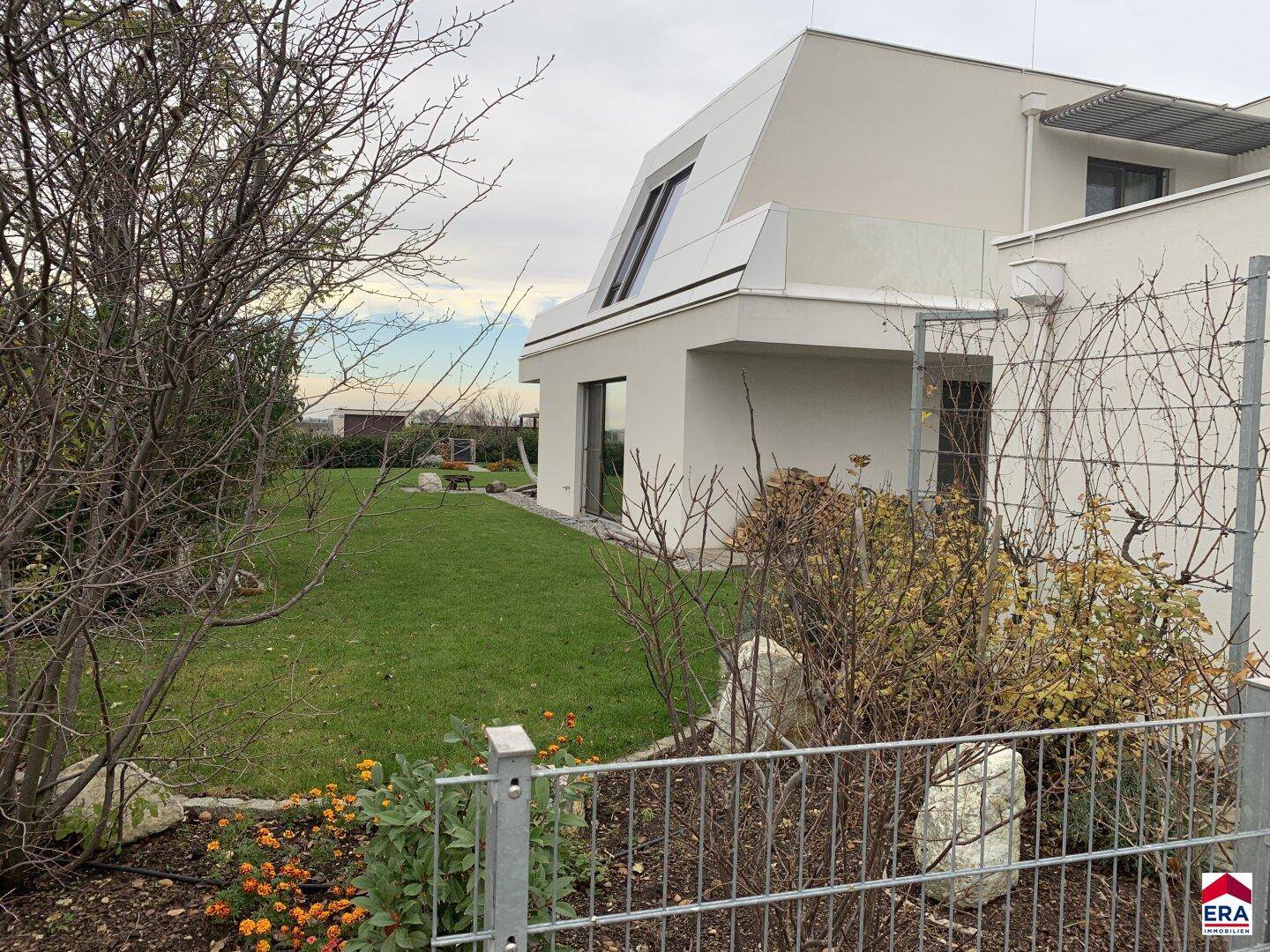Seitlicher Gartenbereich mit Rasenfläche, Bäumen und Blick auf die moderne Architektur des Hauses.
