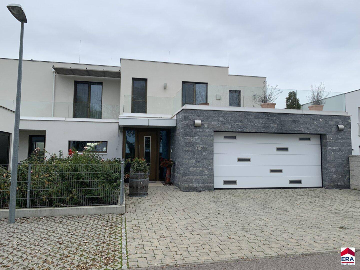 Eingangsbereich der modernen Villa mit Doppelgarage und gepflasterter Auffahrt.