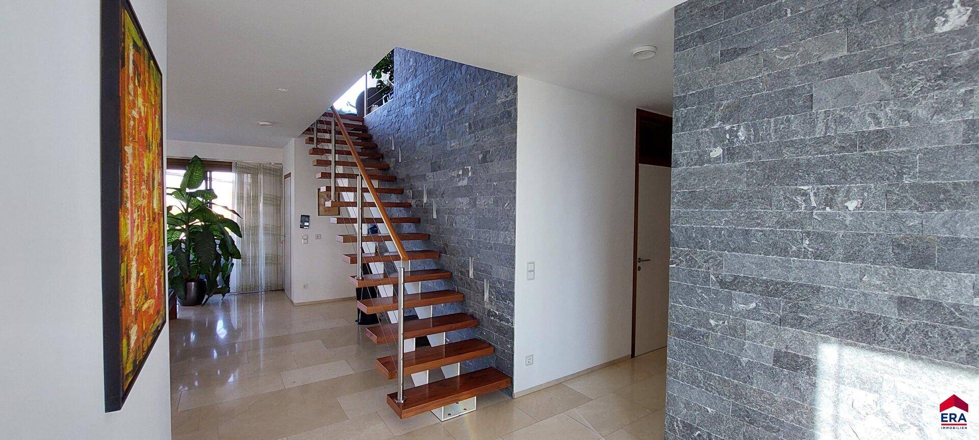 Heller Eingangsbereich mit moderner Holztreppe und einer Wandverkleidung aus Naturstein.