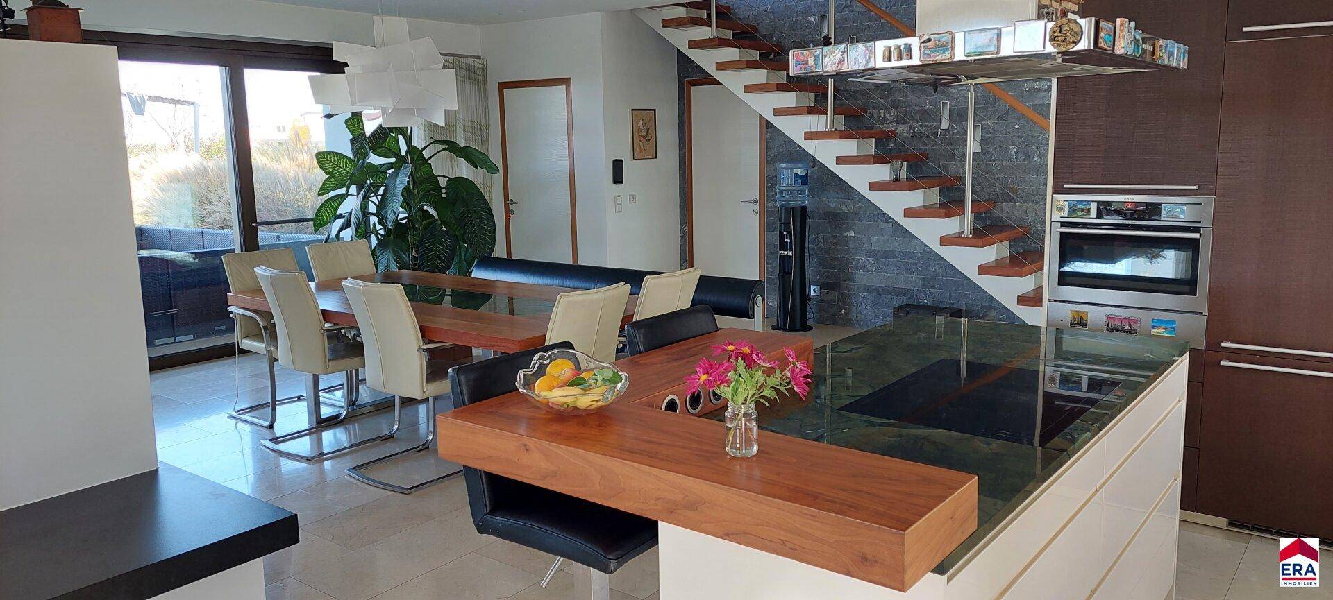 Eleganter Essbereich mit großem Holztisch, modernen Stühlen und Blick auf die Treppe.
