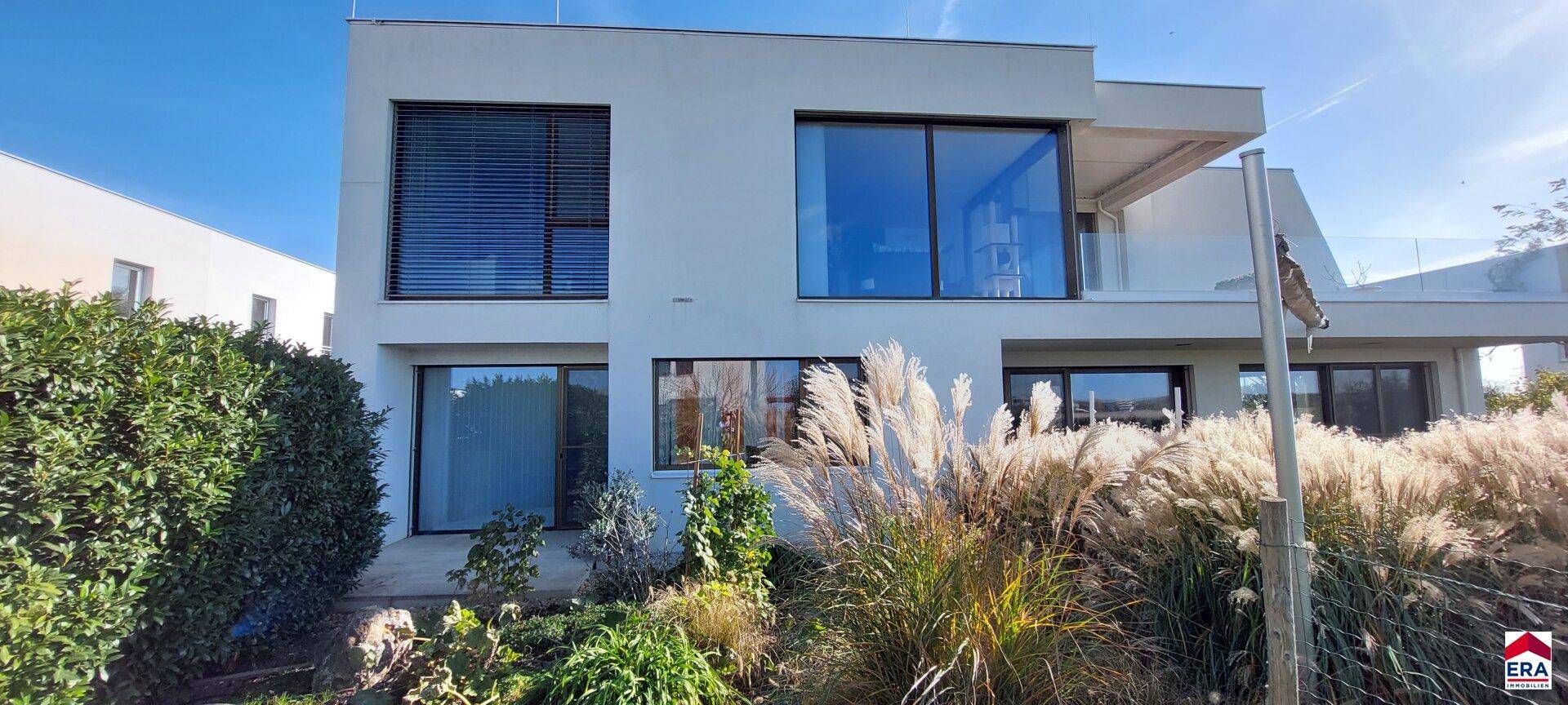 Moderne Hausfassade mit großen Fensterfronten und gepflegter Bepflanzung.