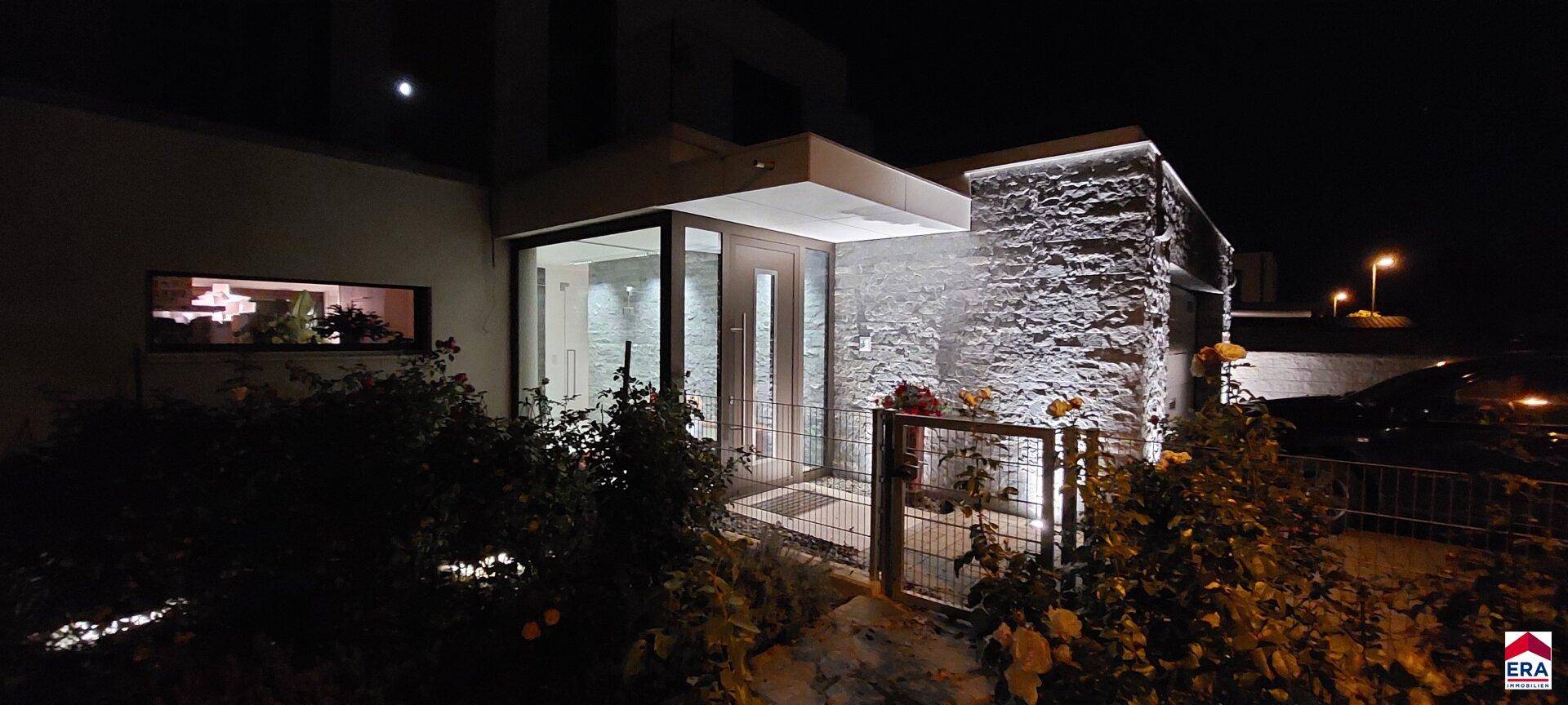 Beleuchteter Eingangsbereich der modernen Villa bei Nacht mit Steinverkleidung.