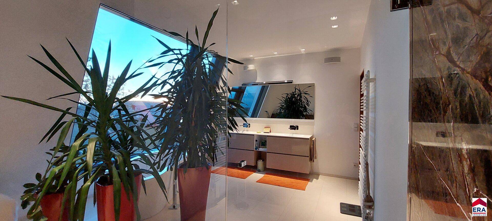 Geräumiges Badezimmer mit großen Fenstern, Pflanzen und modernem Waschtisch.