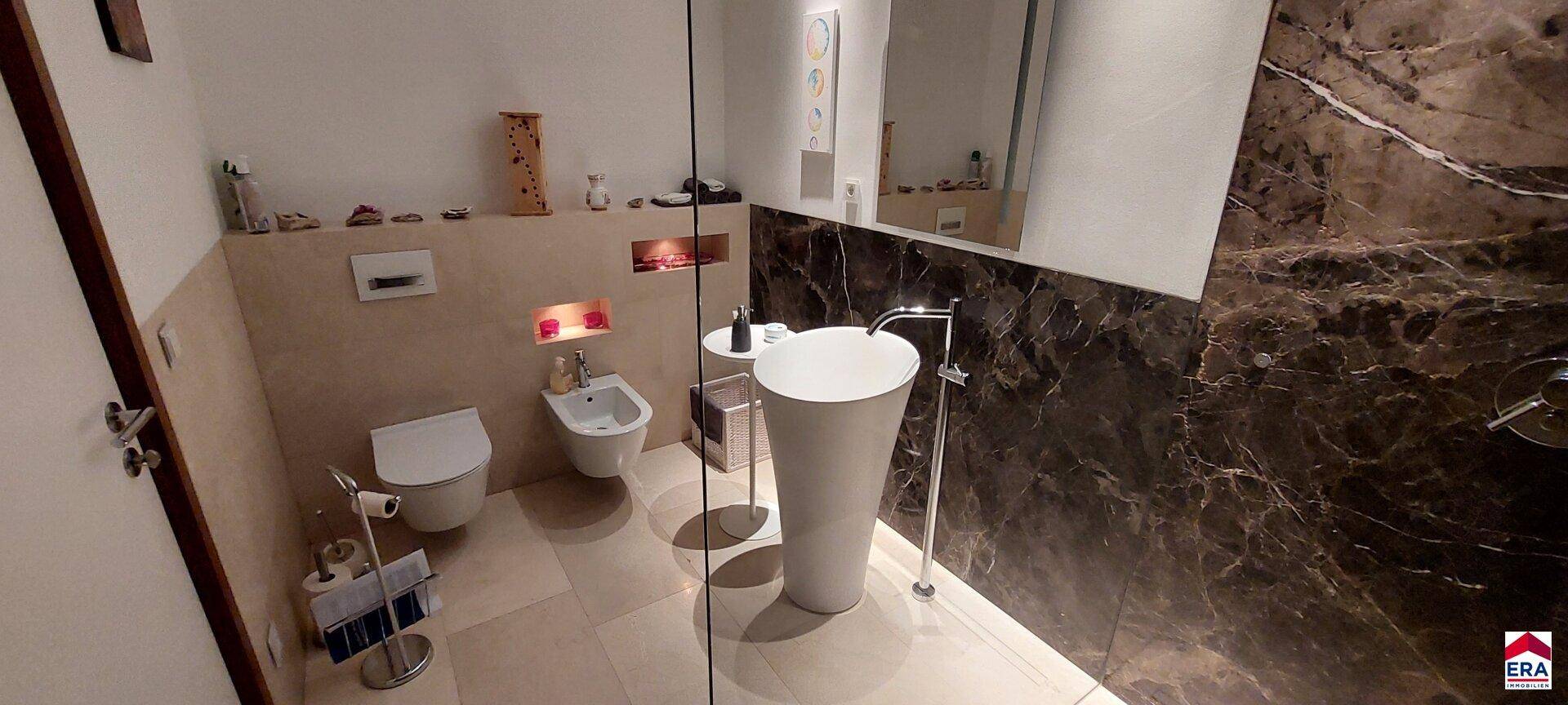 Elegantes Badezimmer mit modernem Waschtisch, Bidet und dunklen Marmorfliesen.