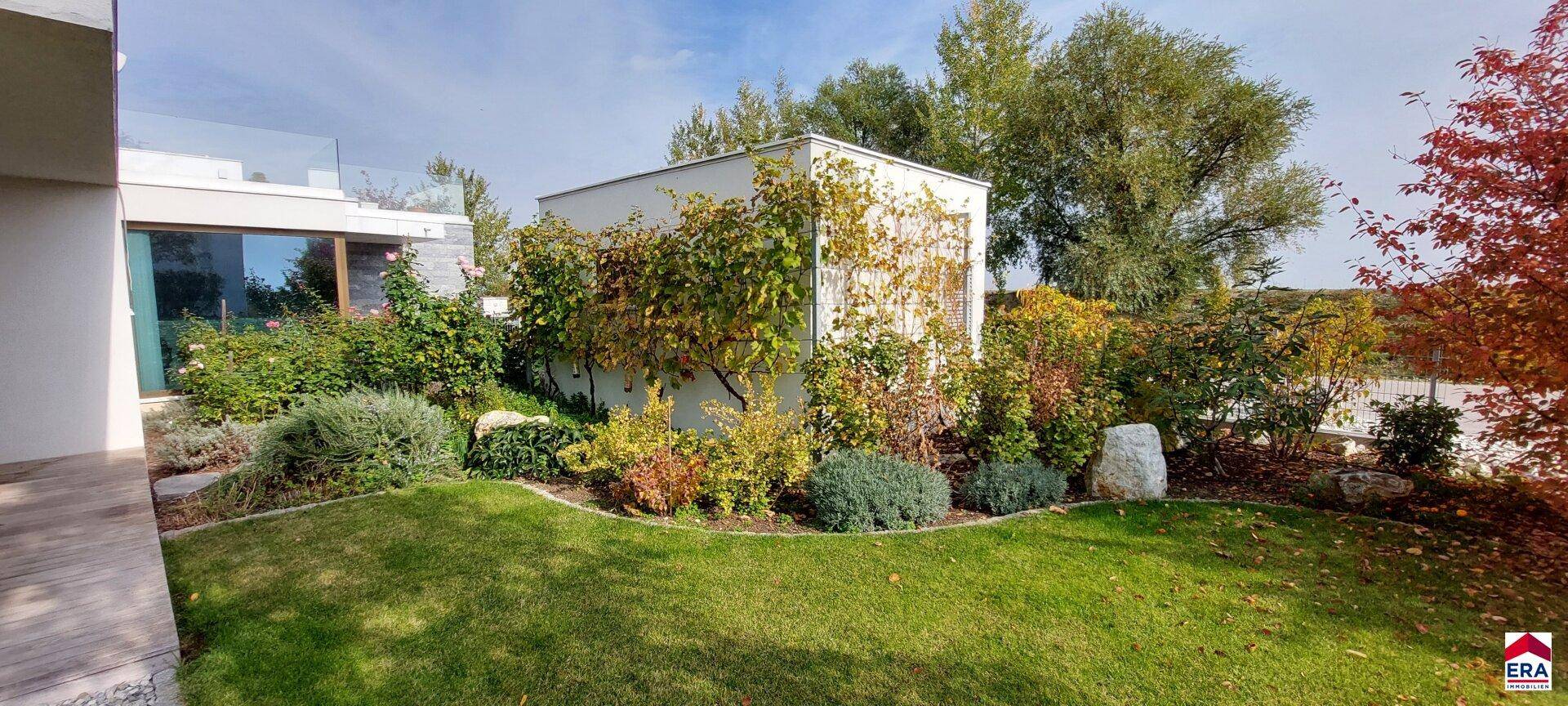 Gepflegter Gartenbereich mit vielfältiger Bepflanzung, Rasenfläche und einem kleinen Gartenhaus.