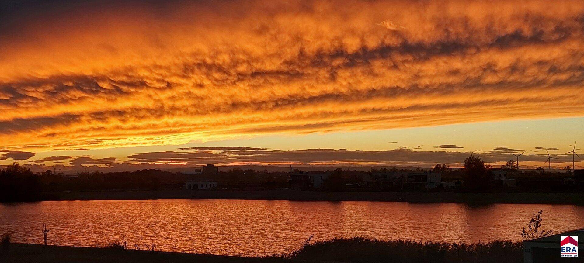 Spektakulärer Sonnenuntergang über dem See mit dramatischen orangefarbenen Wolkenformationen.