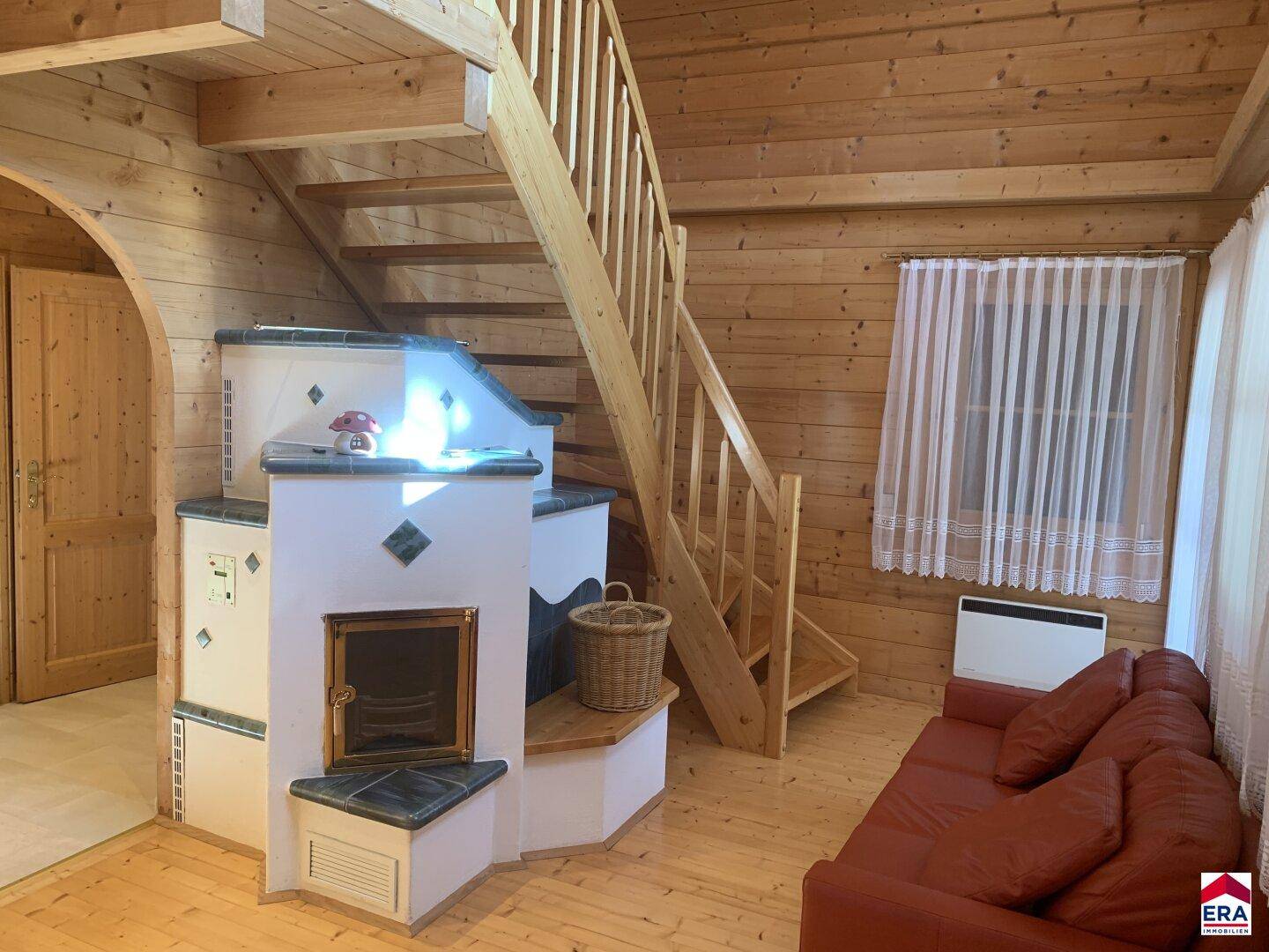 Gemütlicher Wohnbereich mit Holzwänden, Holztreppe und traditionellem Kachelofen.