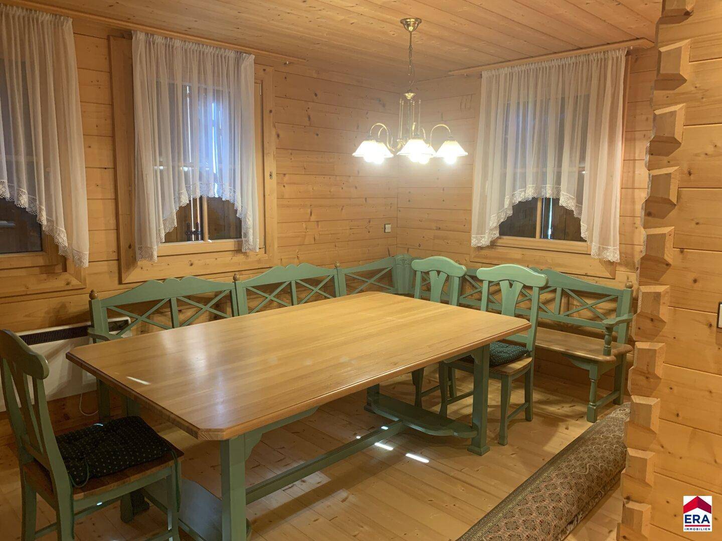 Rustikaler Essbereich mit Holztisch, grünen Stühlen und Holzwänden.