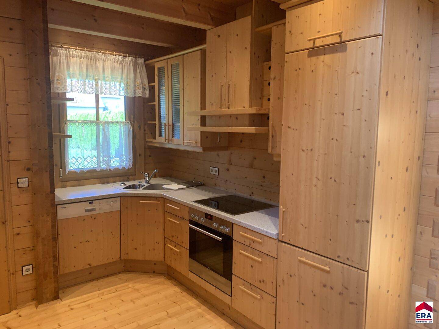 Funktionale Holzküche mit Einbaugeräten, Spüle und Fensterblick ins Grüne.