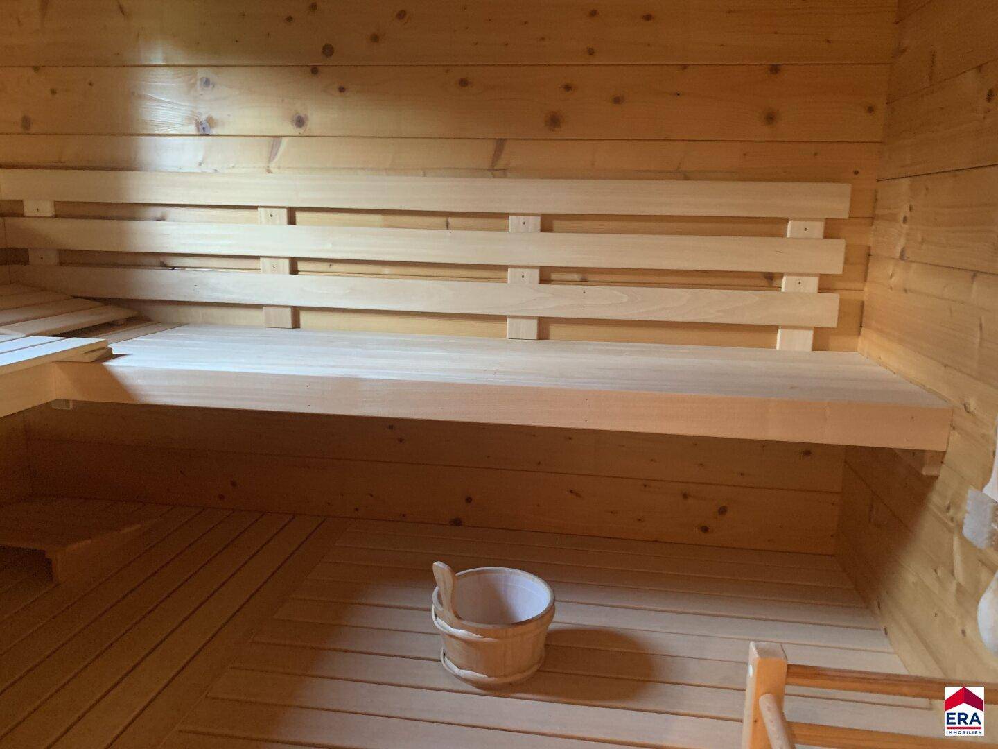 Innenansicht einer traditionellen Holzsauna mit Bänken und Eimer.
